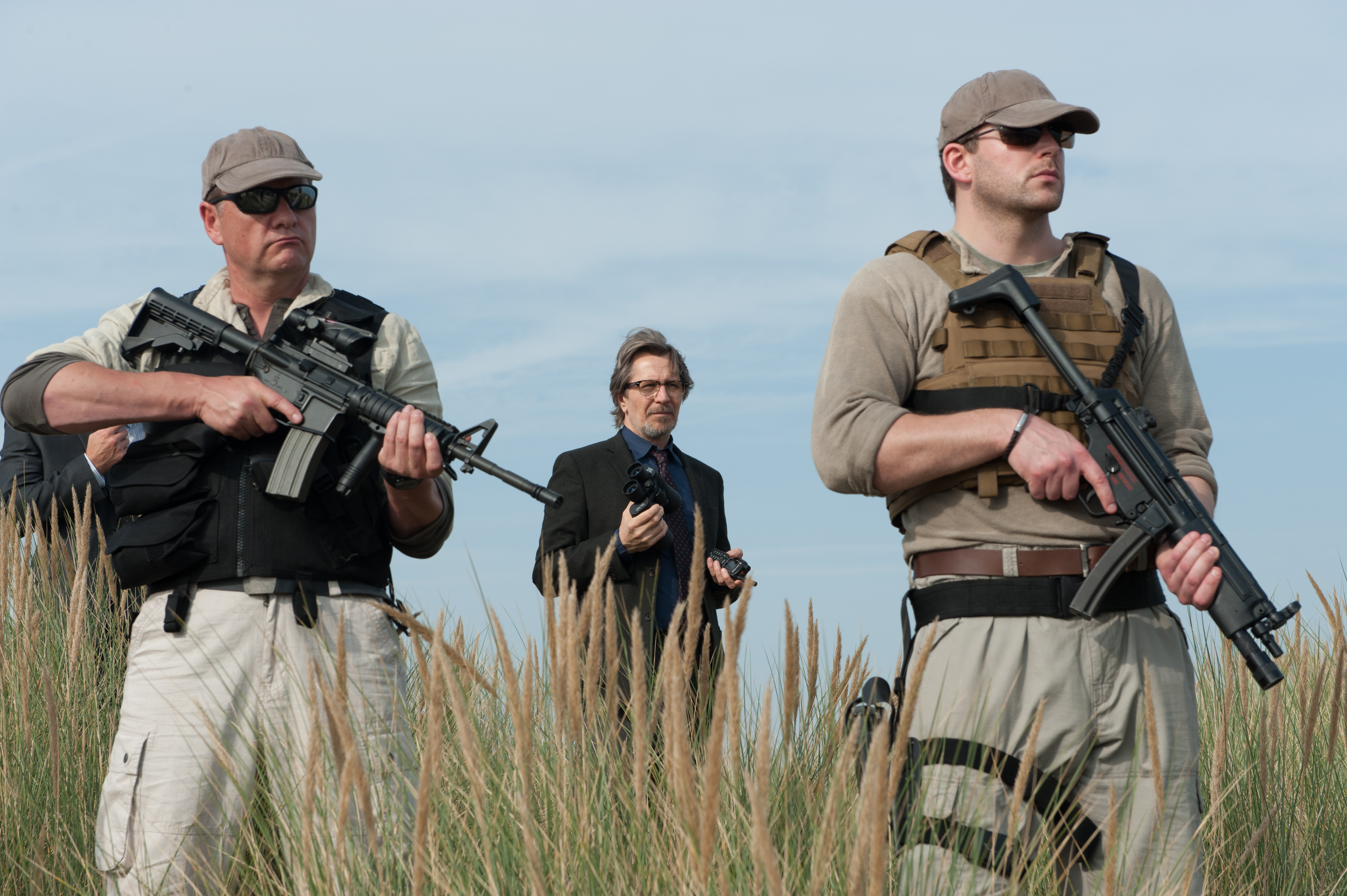 Gary Oldman with armed guards in field HD Wallpaper