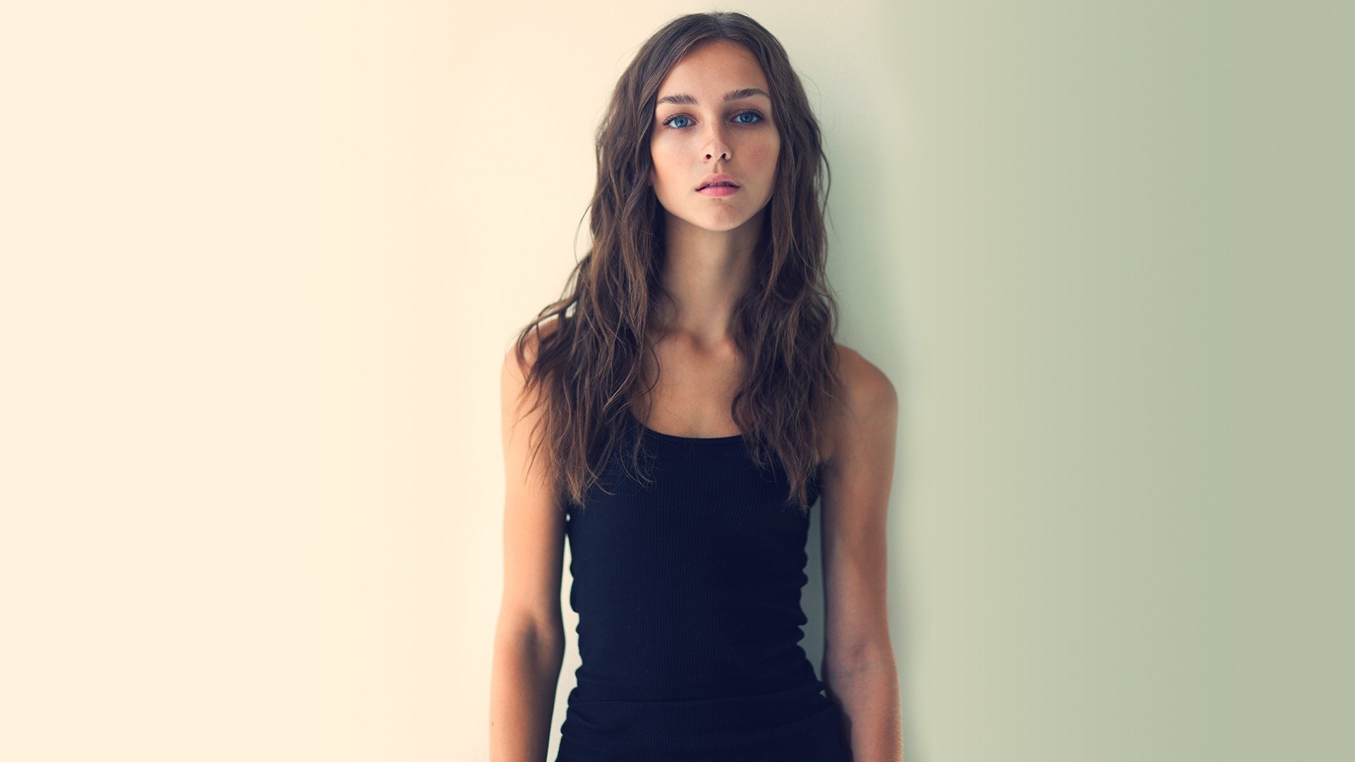 Young woman in black tank top against a wall HD Wallpaper