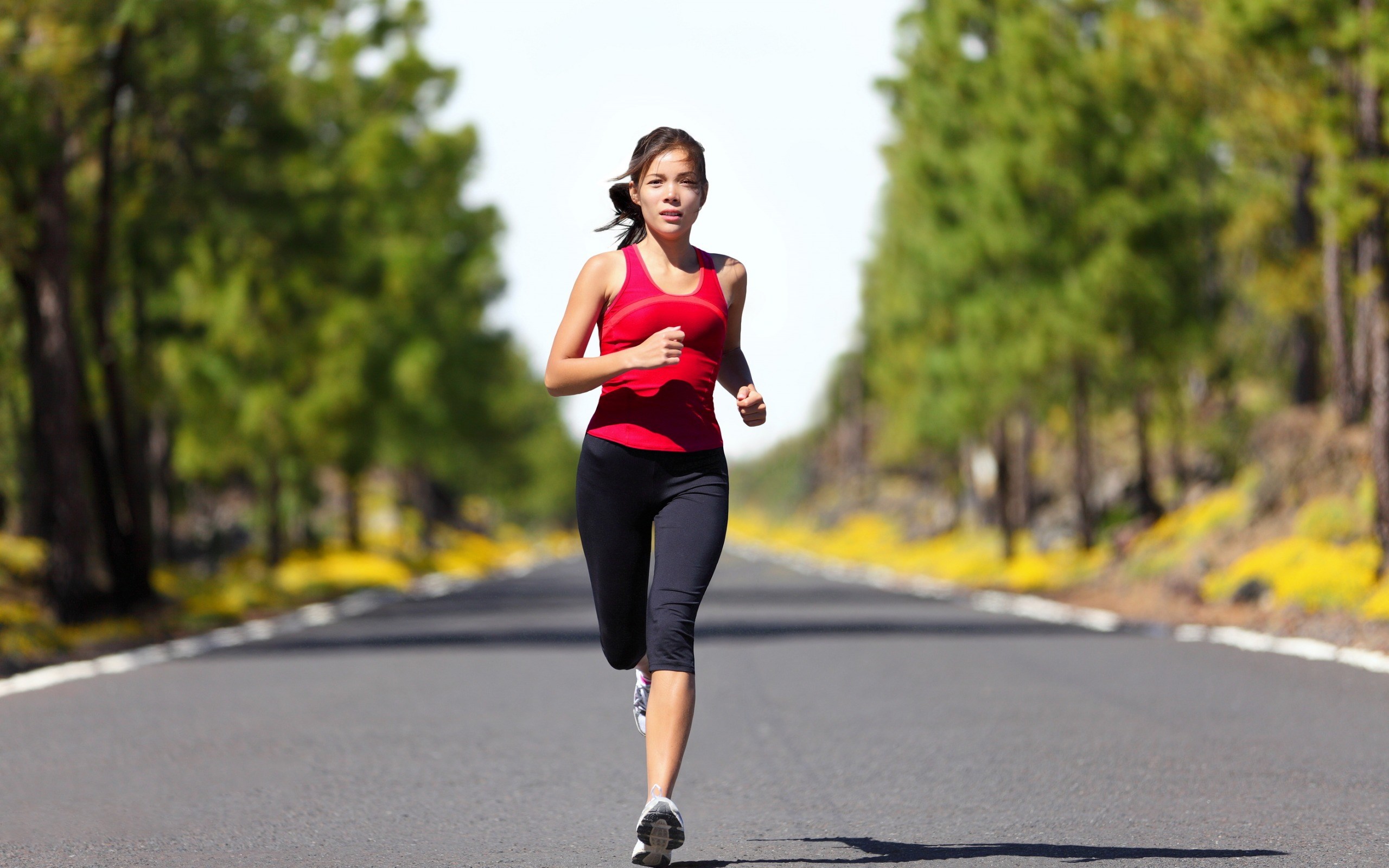 Woman running on a road lined with trees HD Wallpaper
