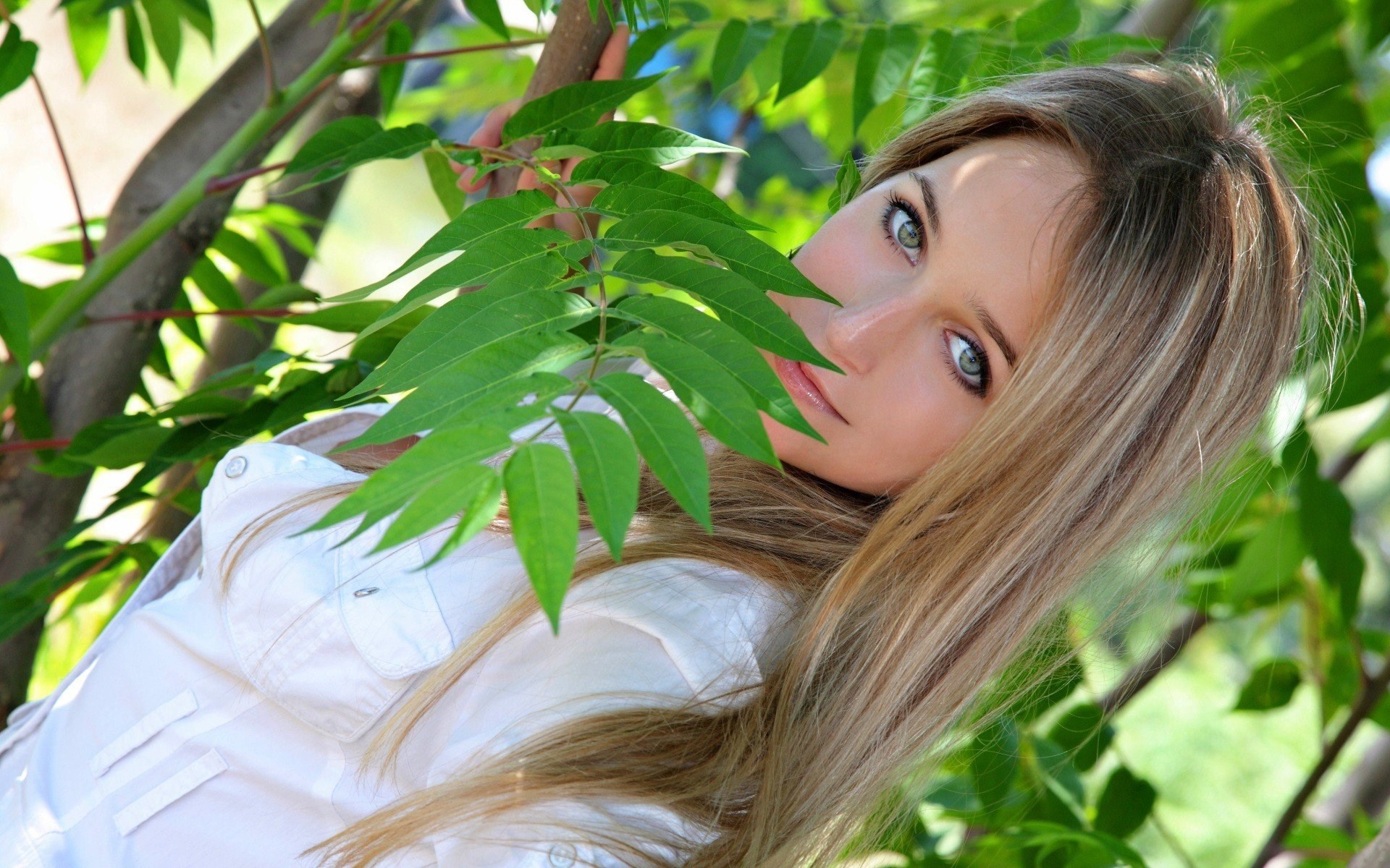 Woman peeking through green leaves HD Wallpaper