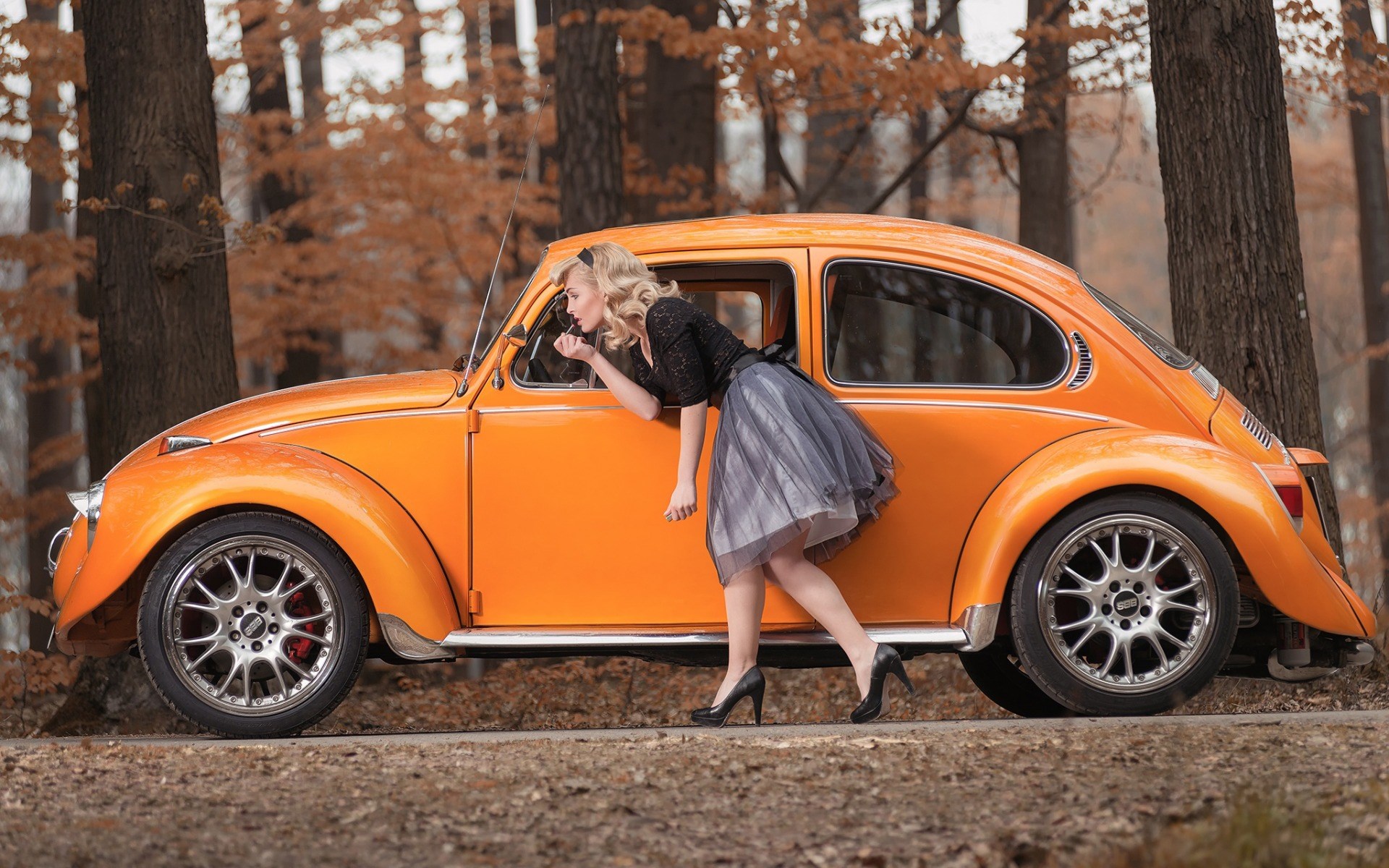 Woman applying makeup in an orange Volkswagen Beetle HD Wallpaper