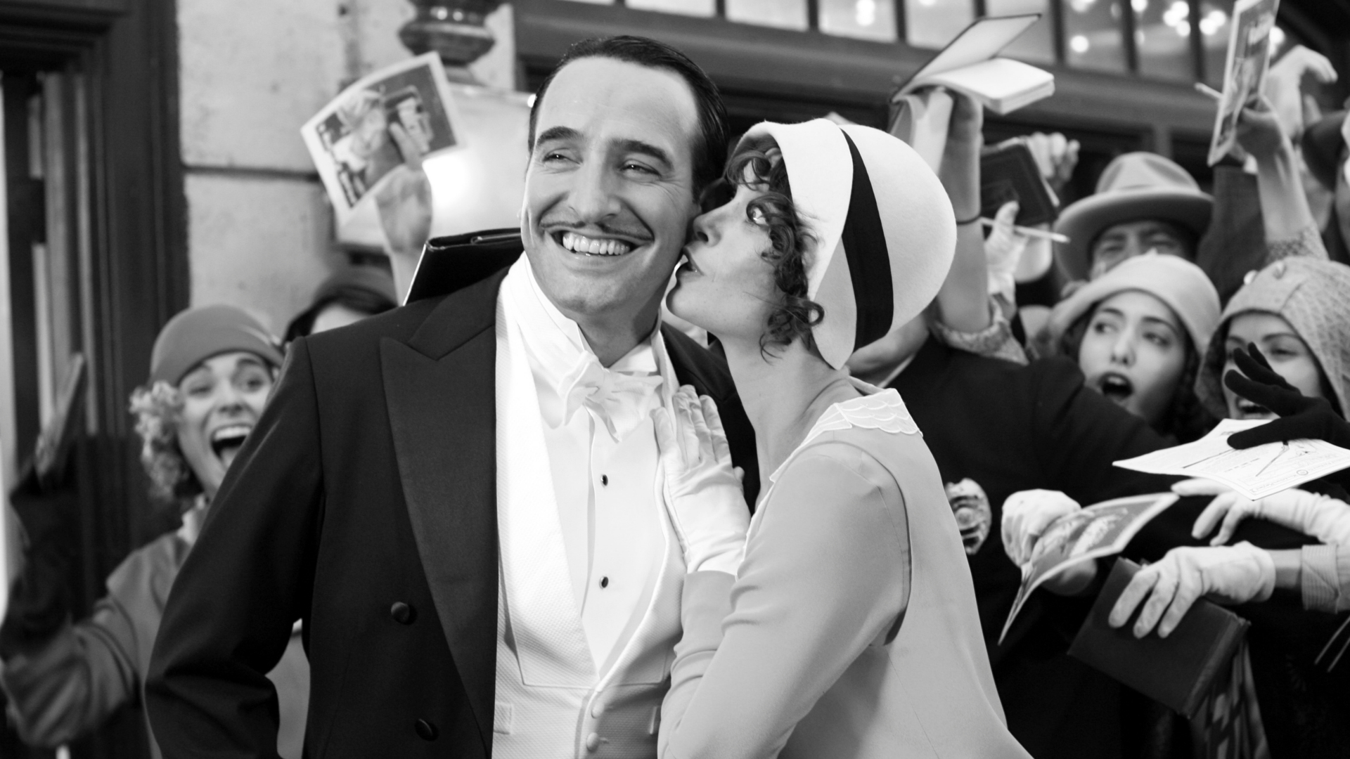 Jean Dujardin in a tuxedo with a woman kissing him HD Wallpaper