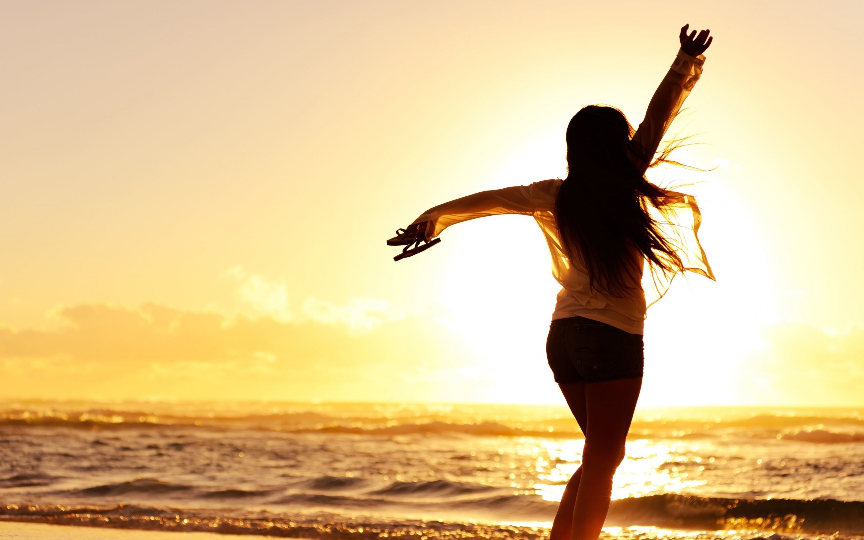 Woman with arms outstretched on a beach at sunset HD Wallpaper