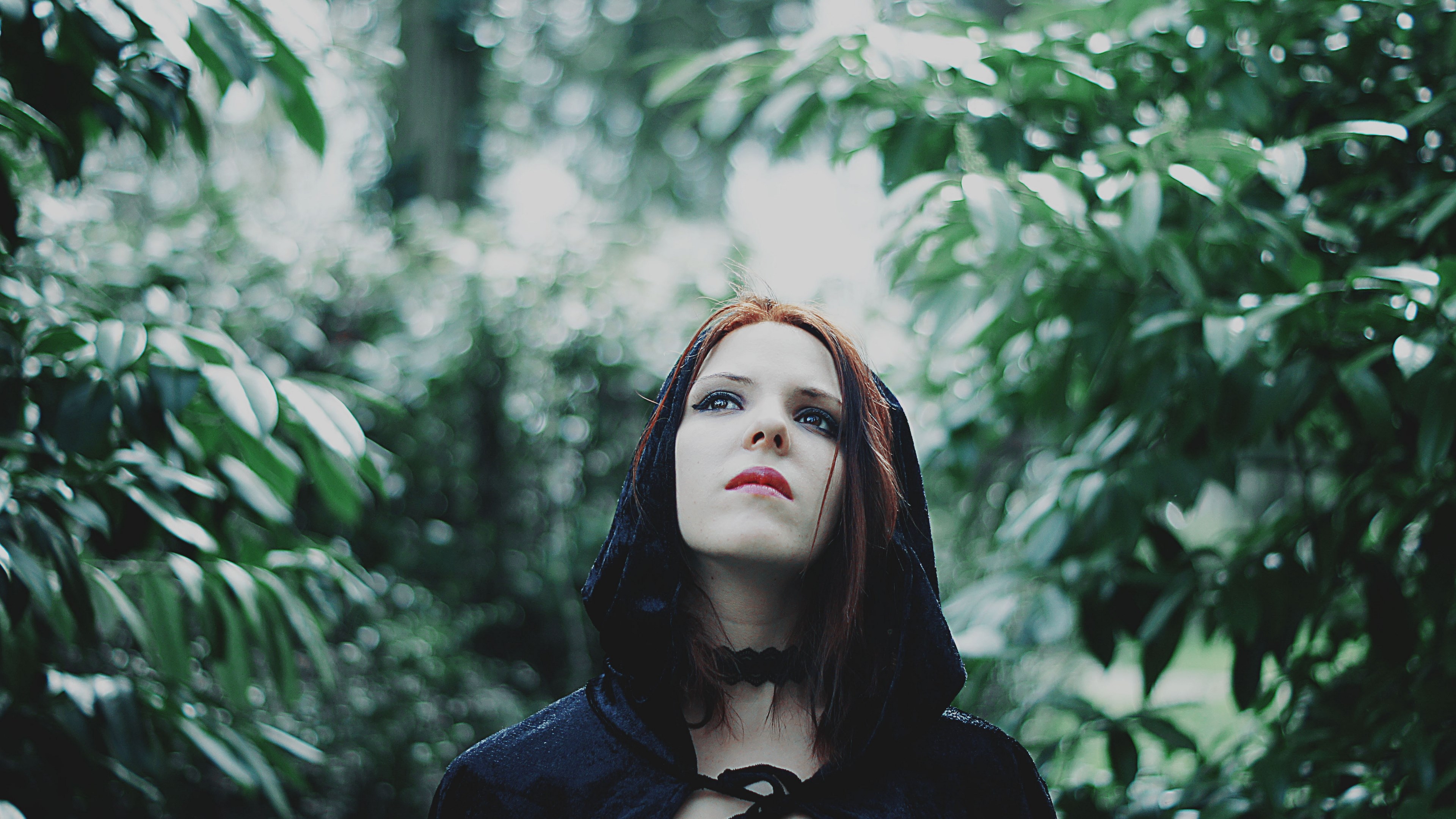 Woman in a black hood looking up in a forest HD Wallpaper