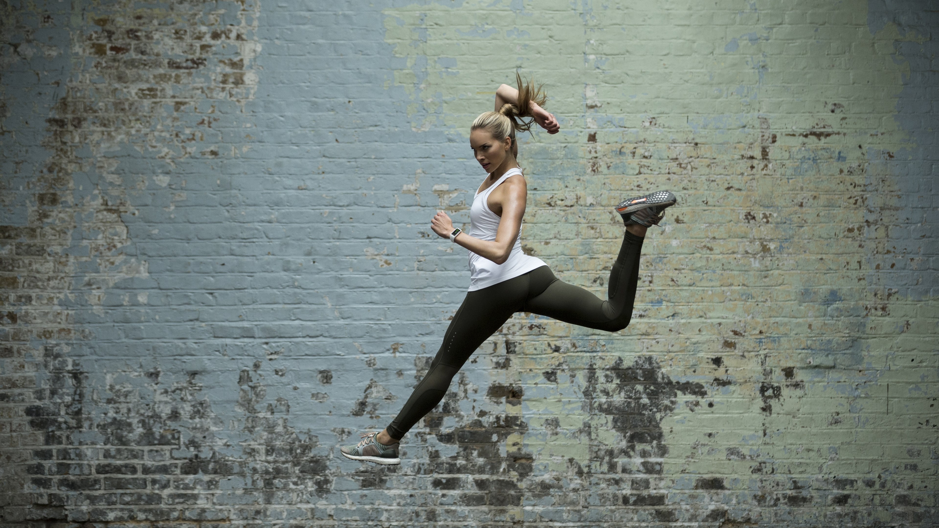 Woman in athletic wear jumping in front of a brick wall HD Wallpaper