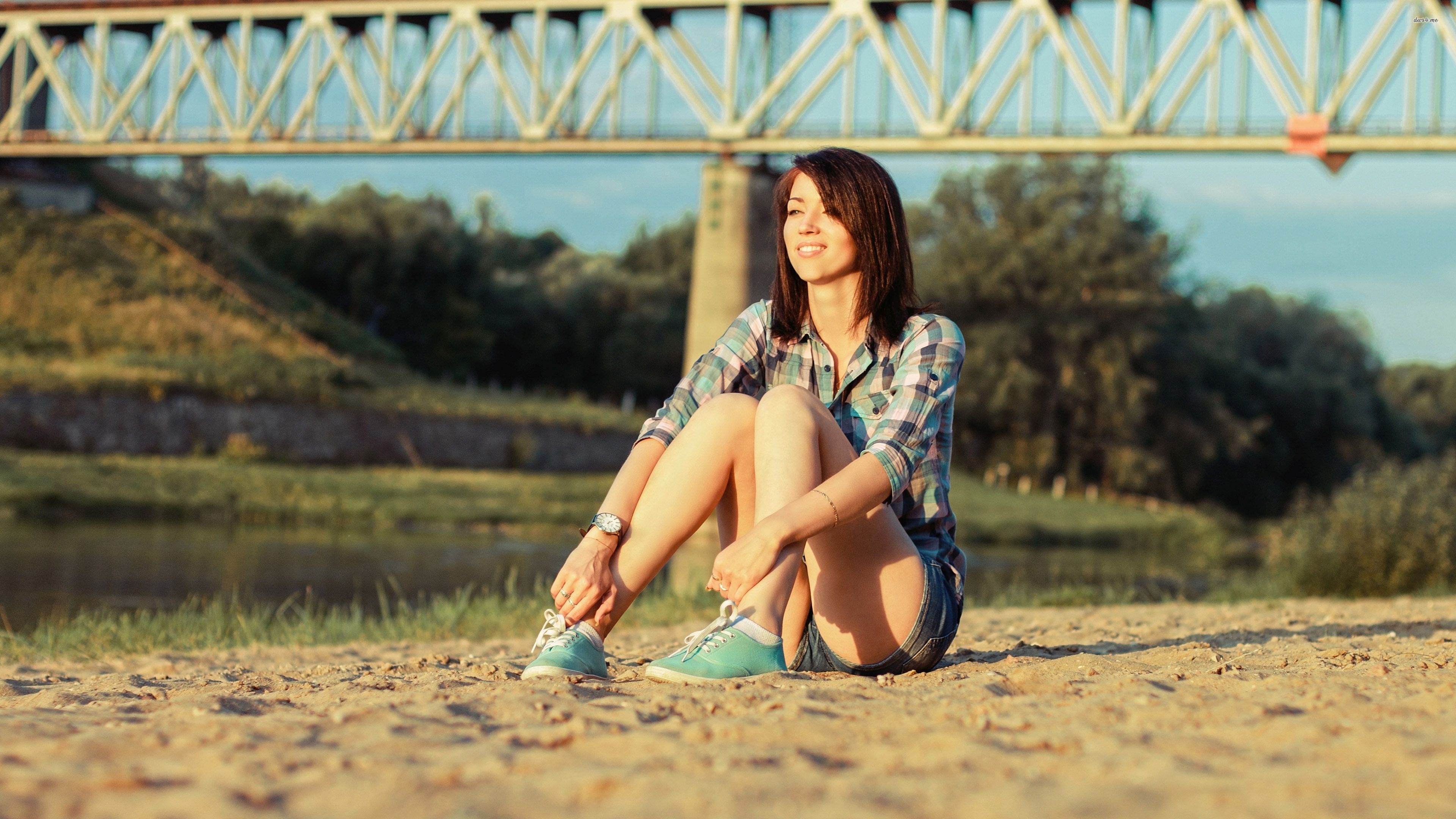 Woman sitting on sand near a bridge HD Wallpaper