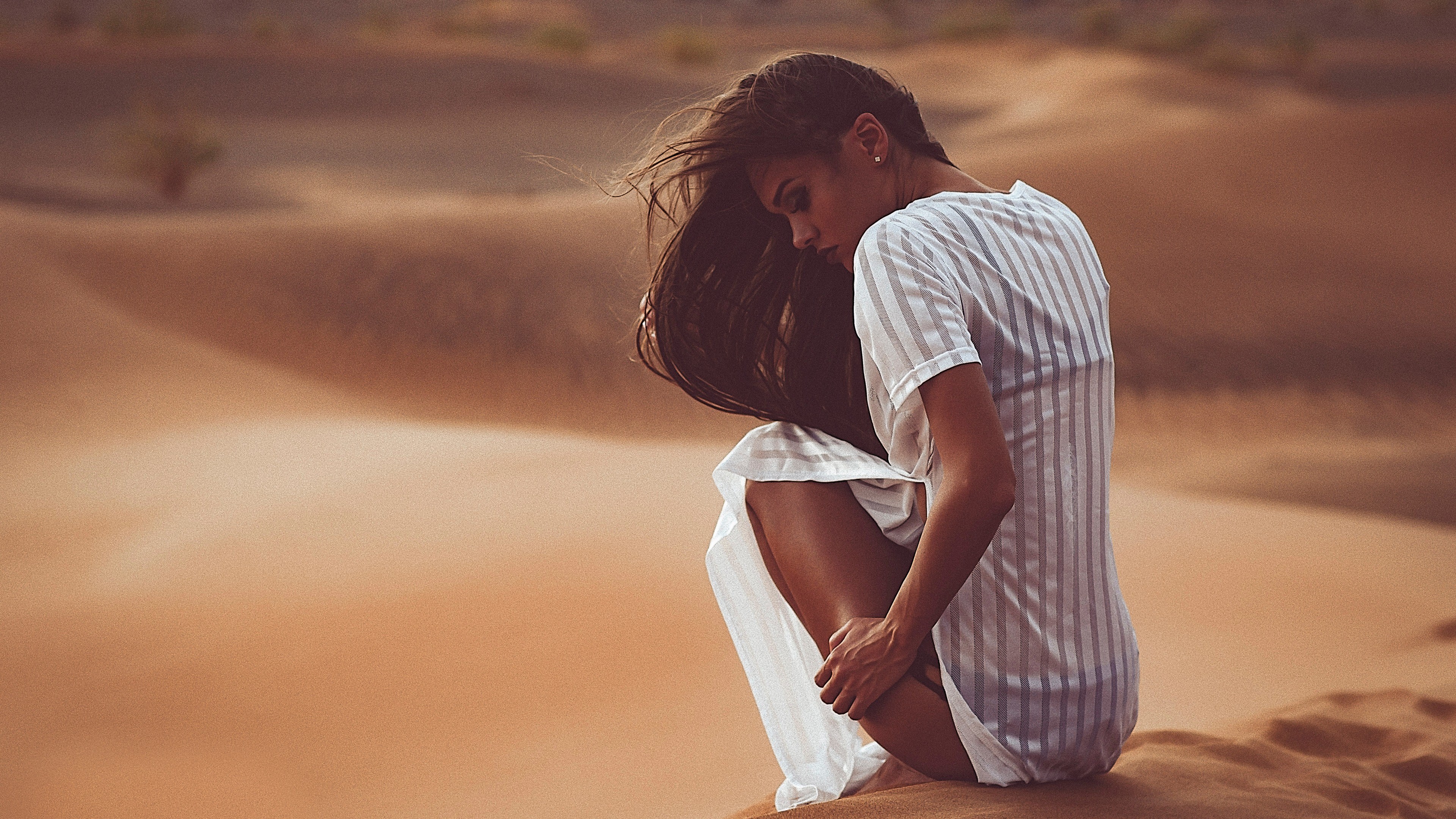 Woman in white dress crouching in desert dunes HD Wallpaper