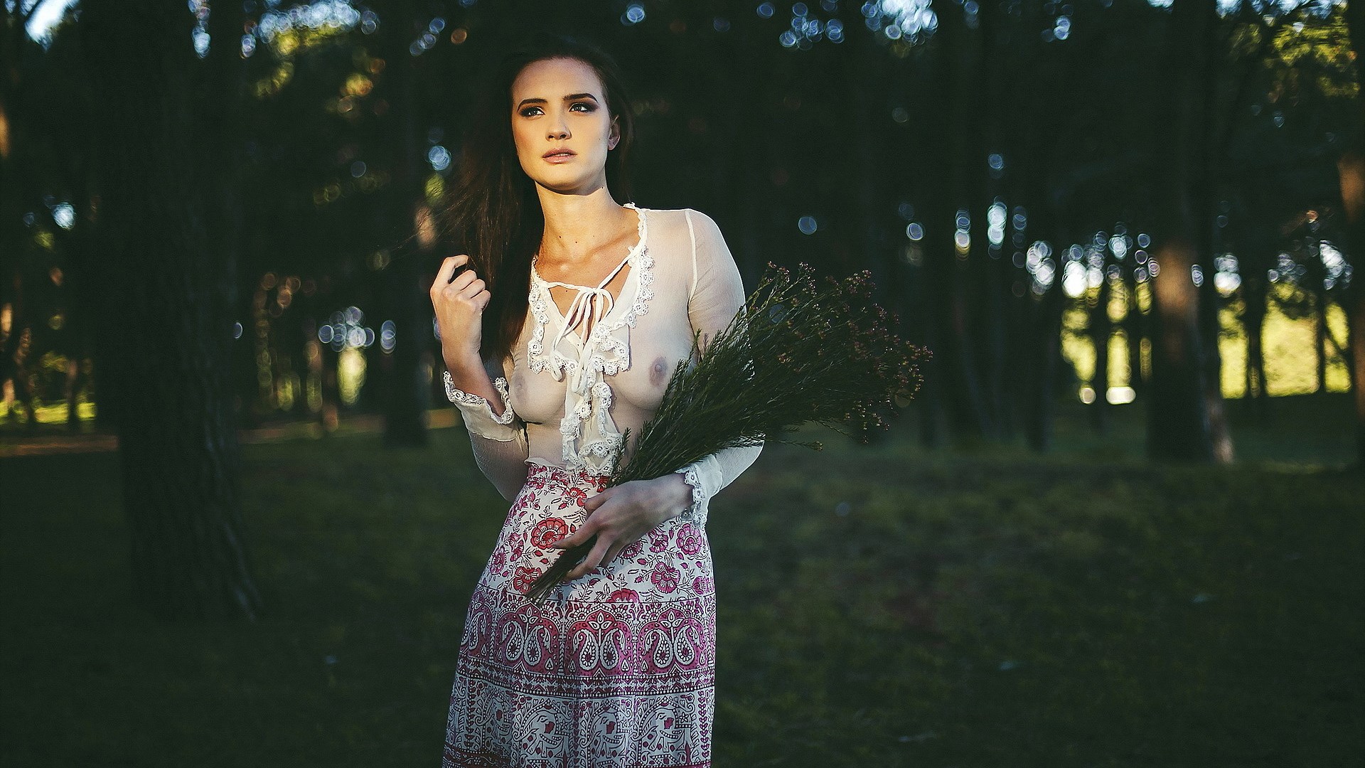 Woman in sheer top holding flowers in forest HD Wallpaper