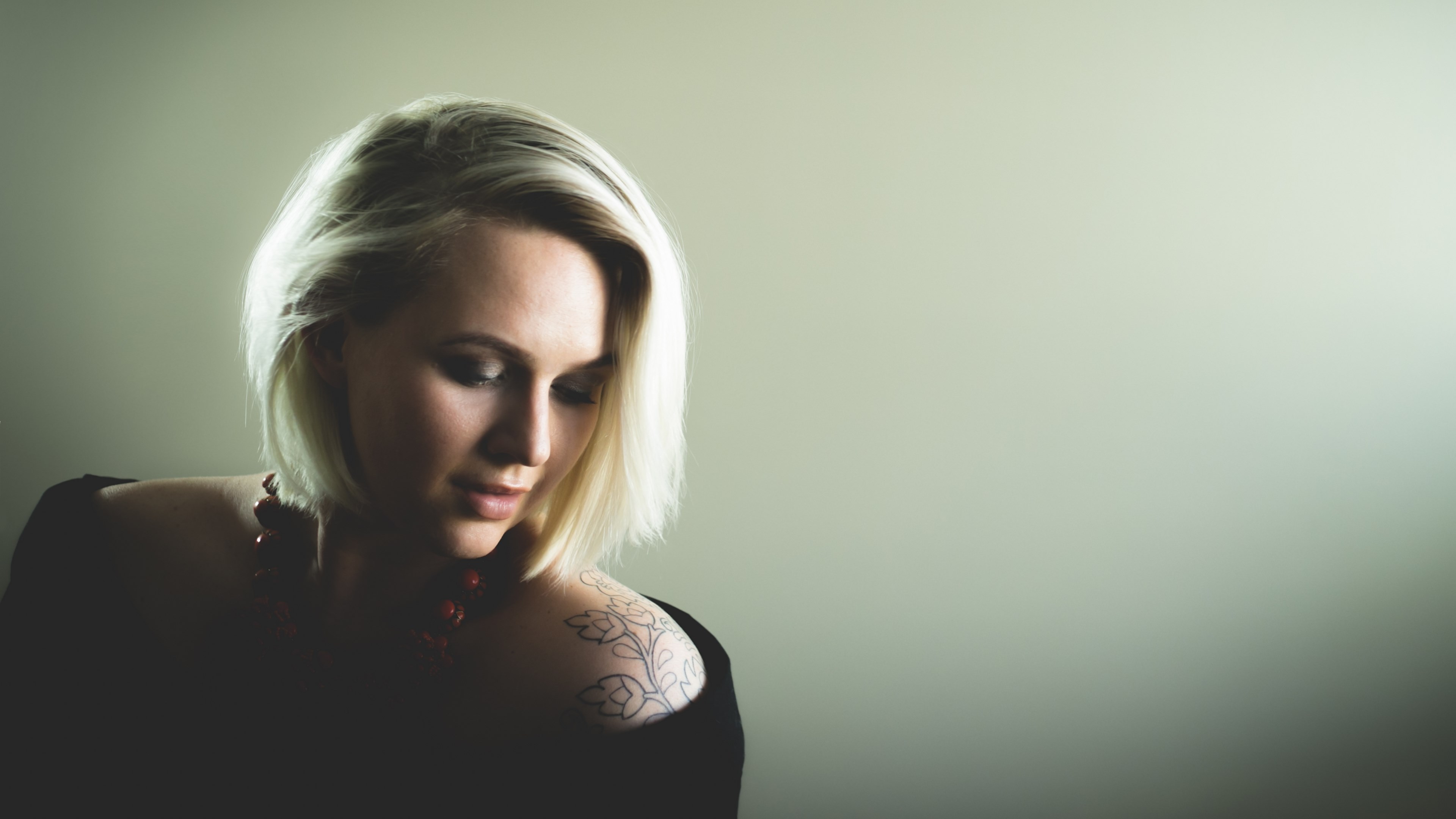 Woman with blonde hair and tattoo looking down HD Wallpaper