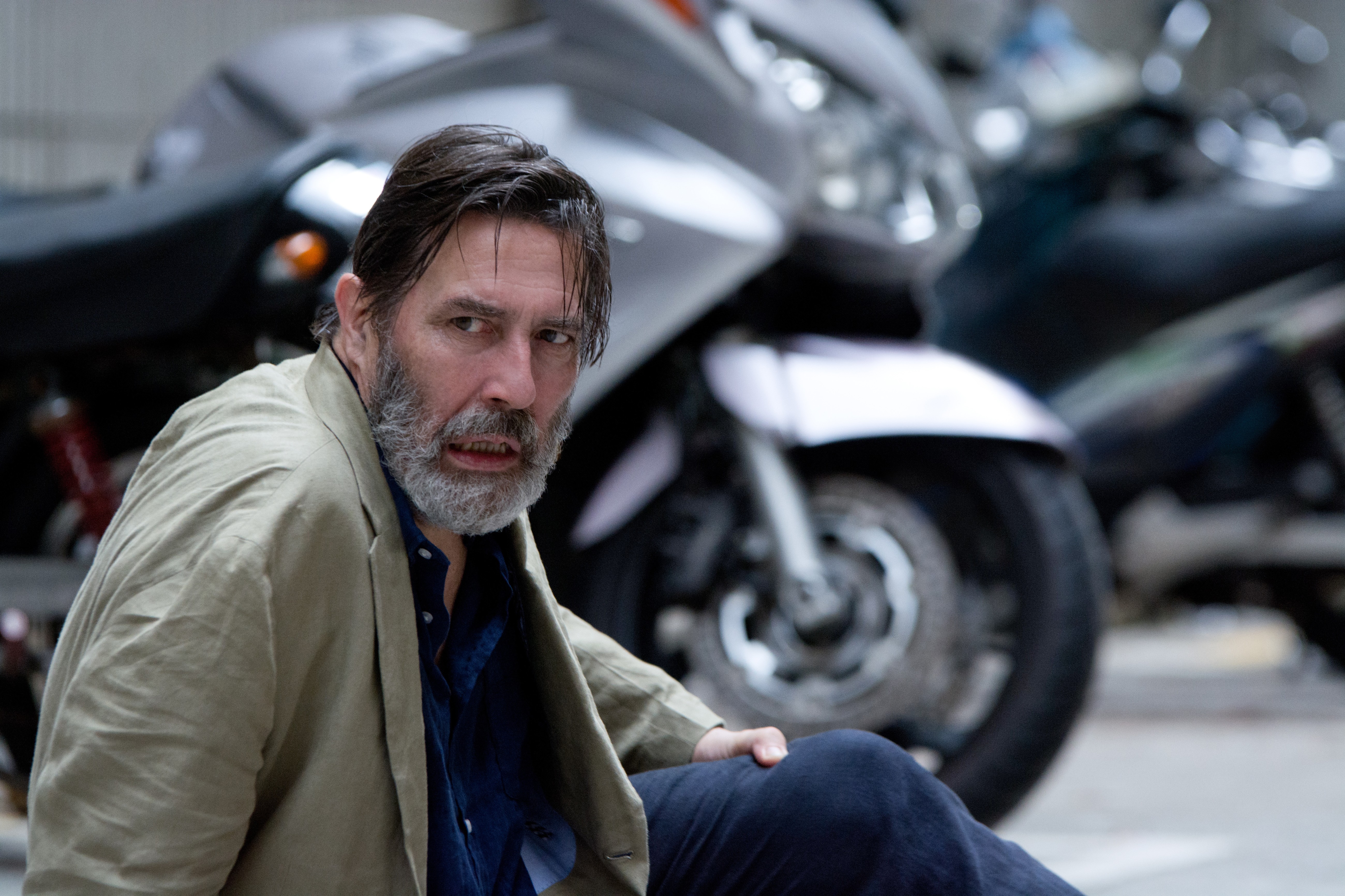 Ciarán Hinds sitting near motorcycles HD Wallpaper