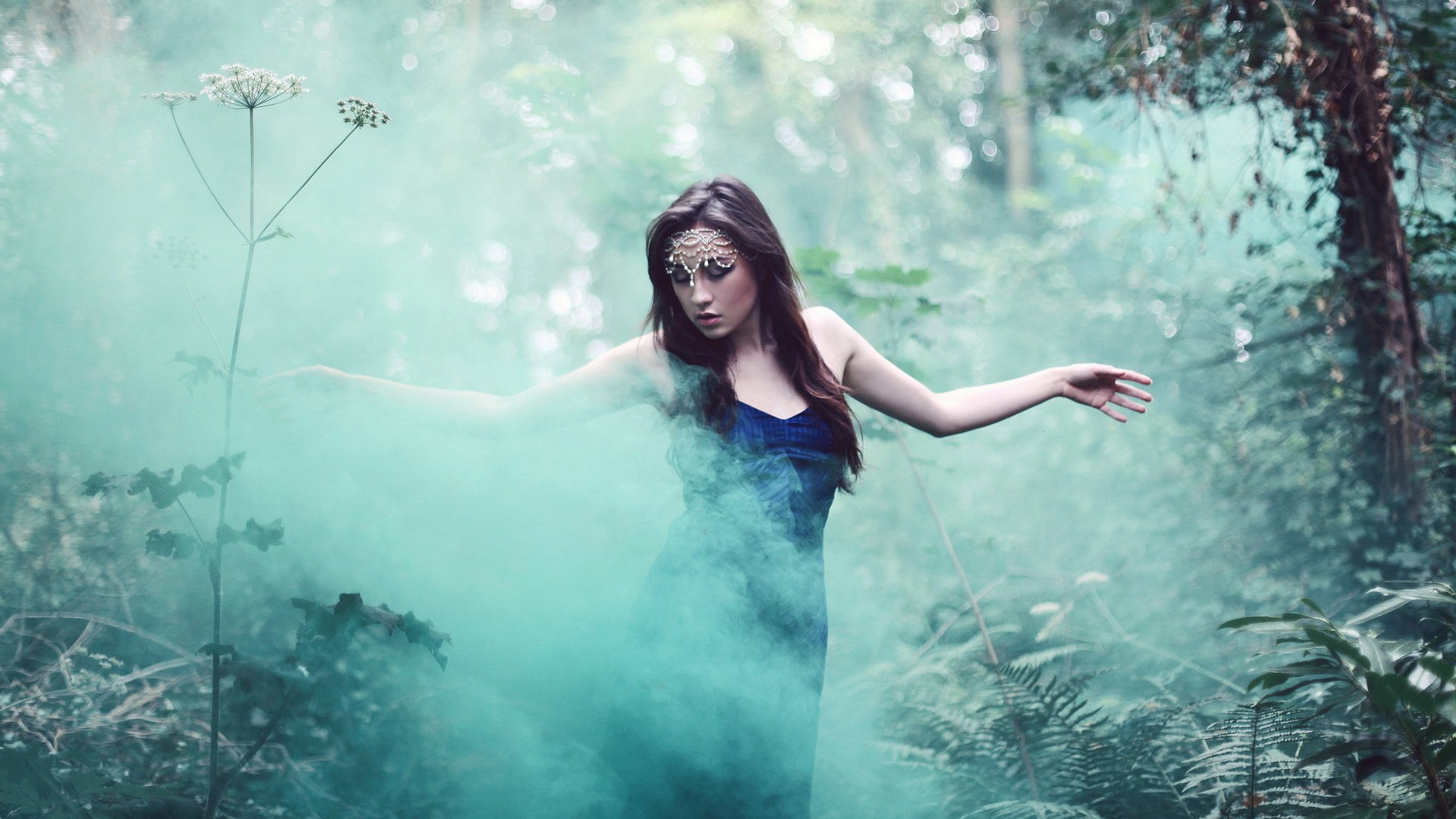 Woman in blue dress with teal smoke in forest HD Wallpaper