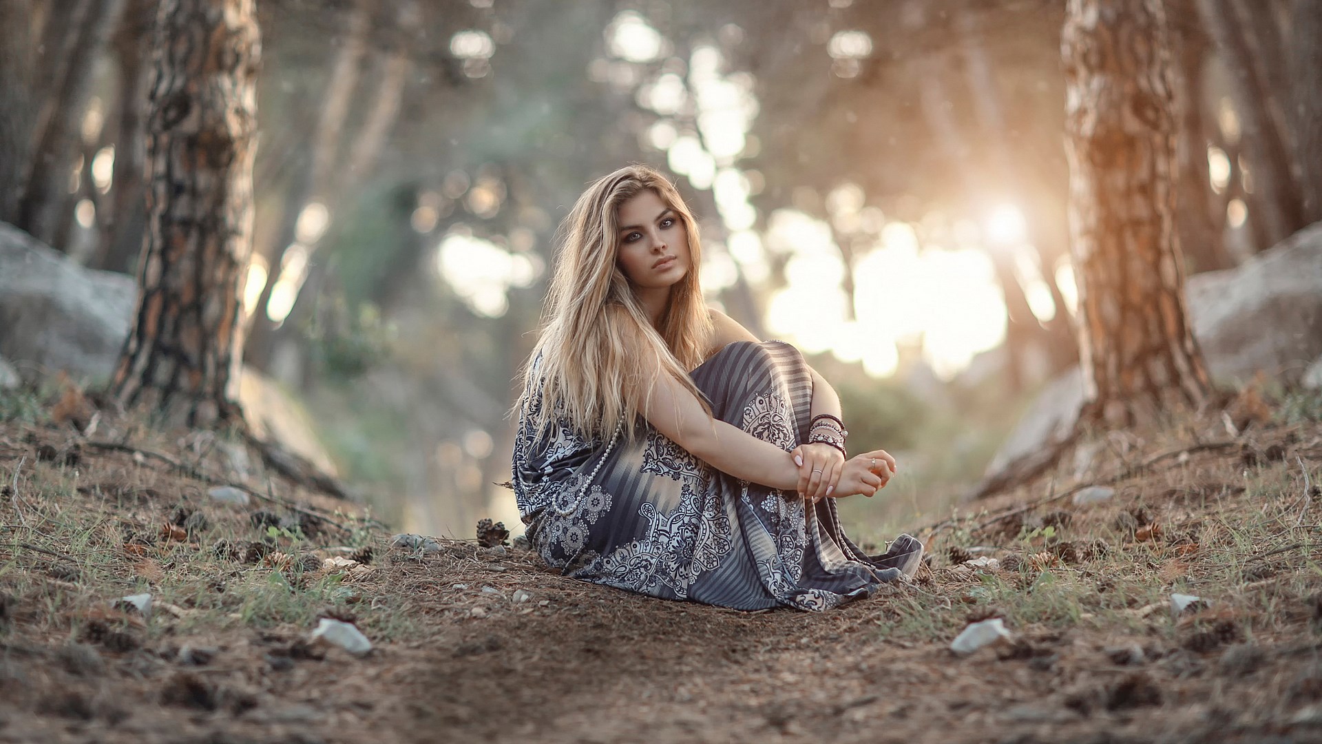 Woman in a patterned dress sitting in a forest HD Wallpaper
