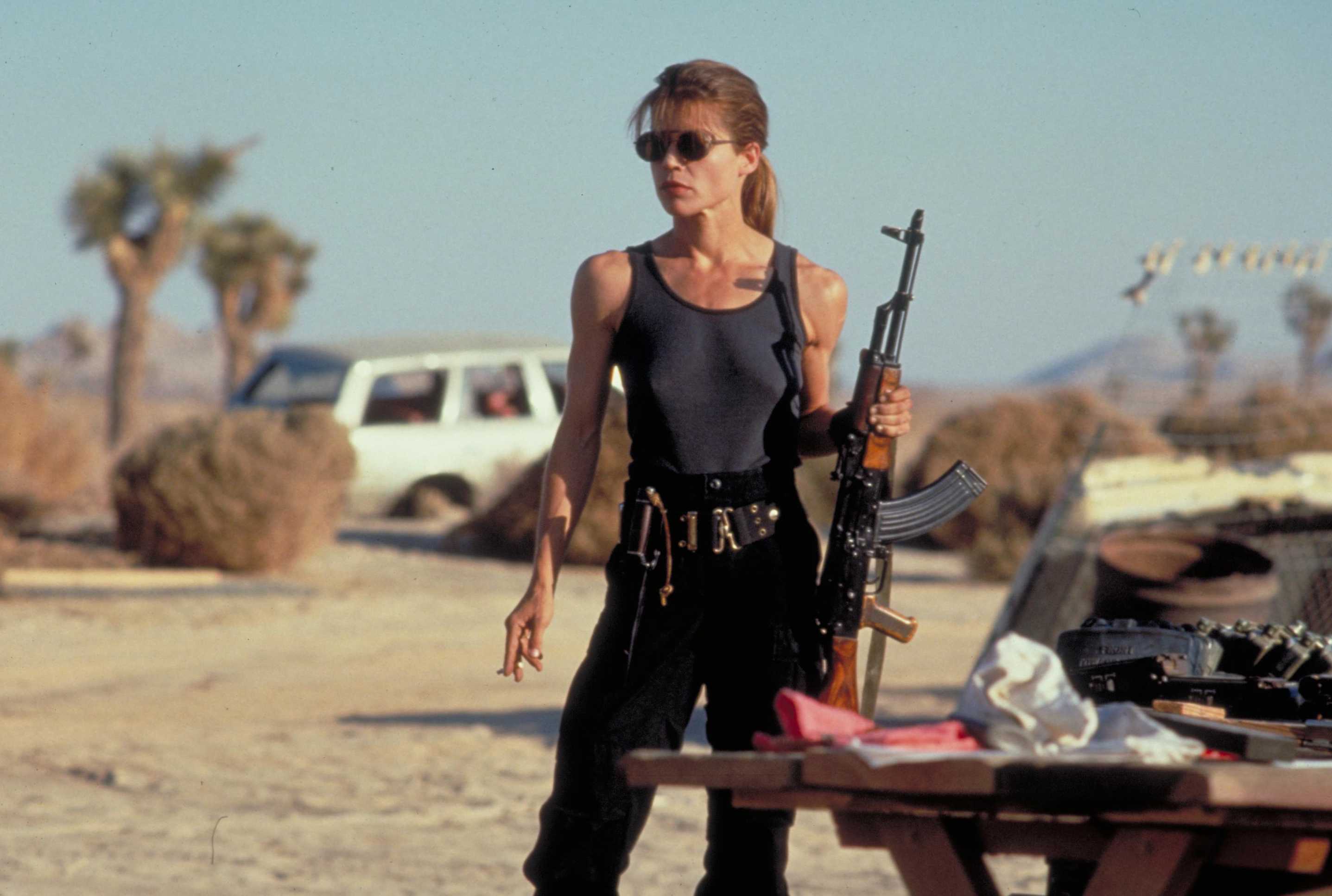 Linda Hamilton holding an AK-47 in a desert HD Wallpaper