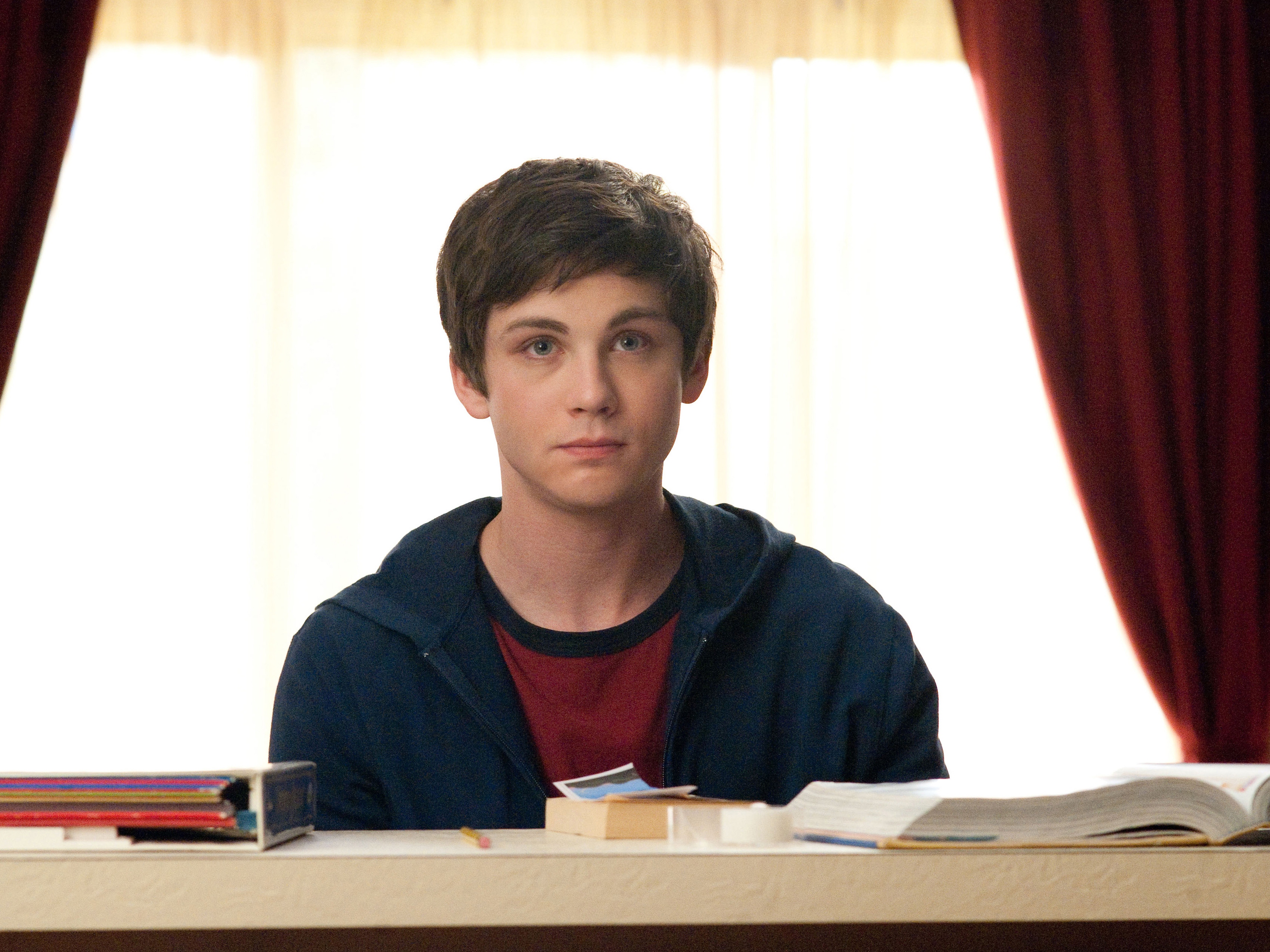 Logan Lerman sitting at a desk HD Wallpaper