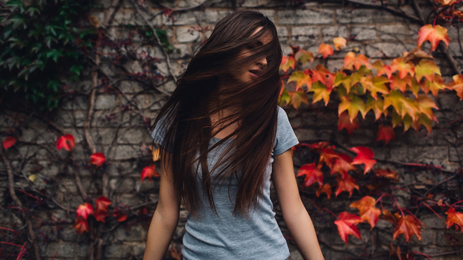 Woman with long brown hair in front of a brick wall with ivy HD Wallpaper