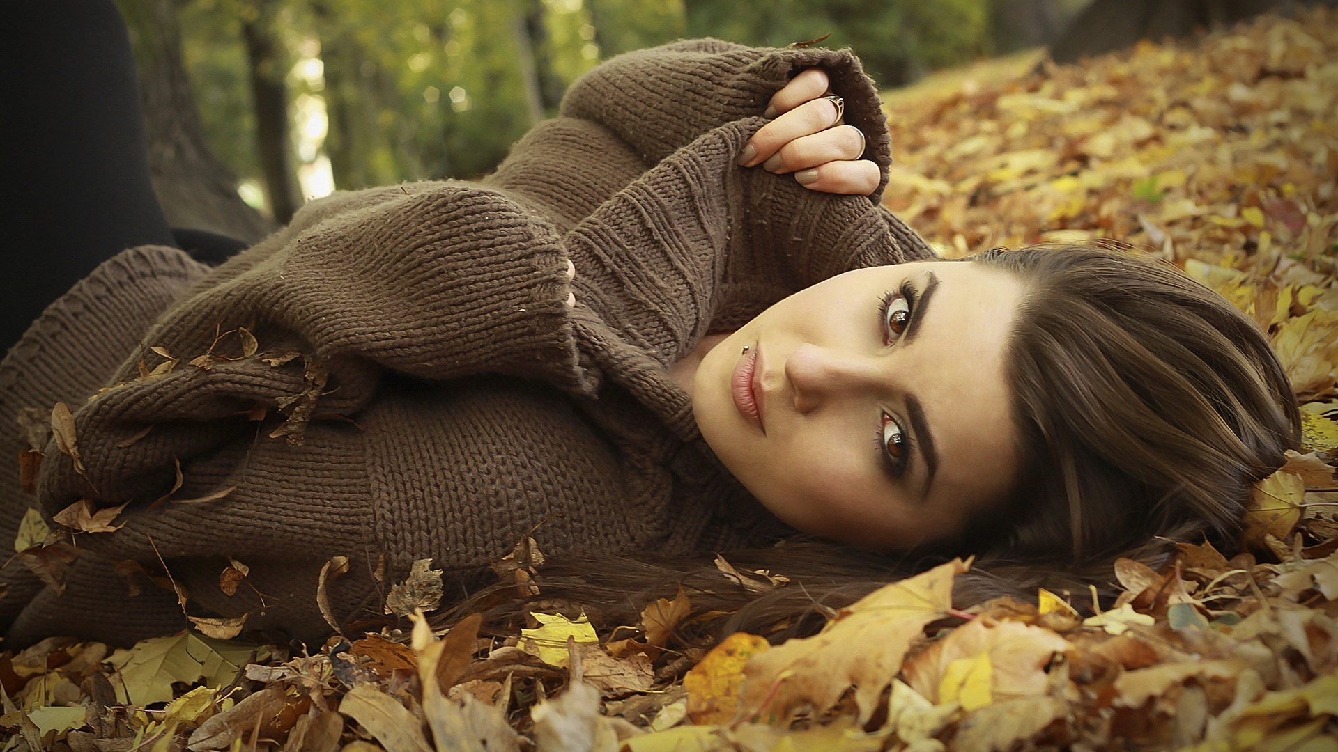 Woman lying in autumn leaves wearing a sweater HD Wallpaper