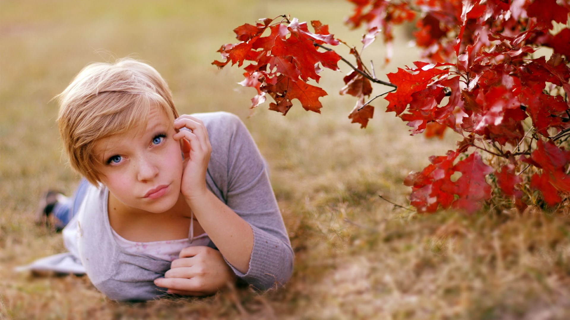 Girl with blue eyes lying on grass near red leaves HD Wallpaper