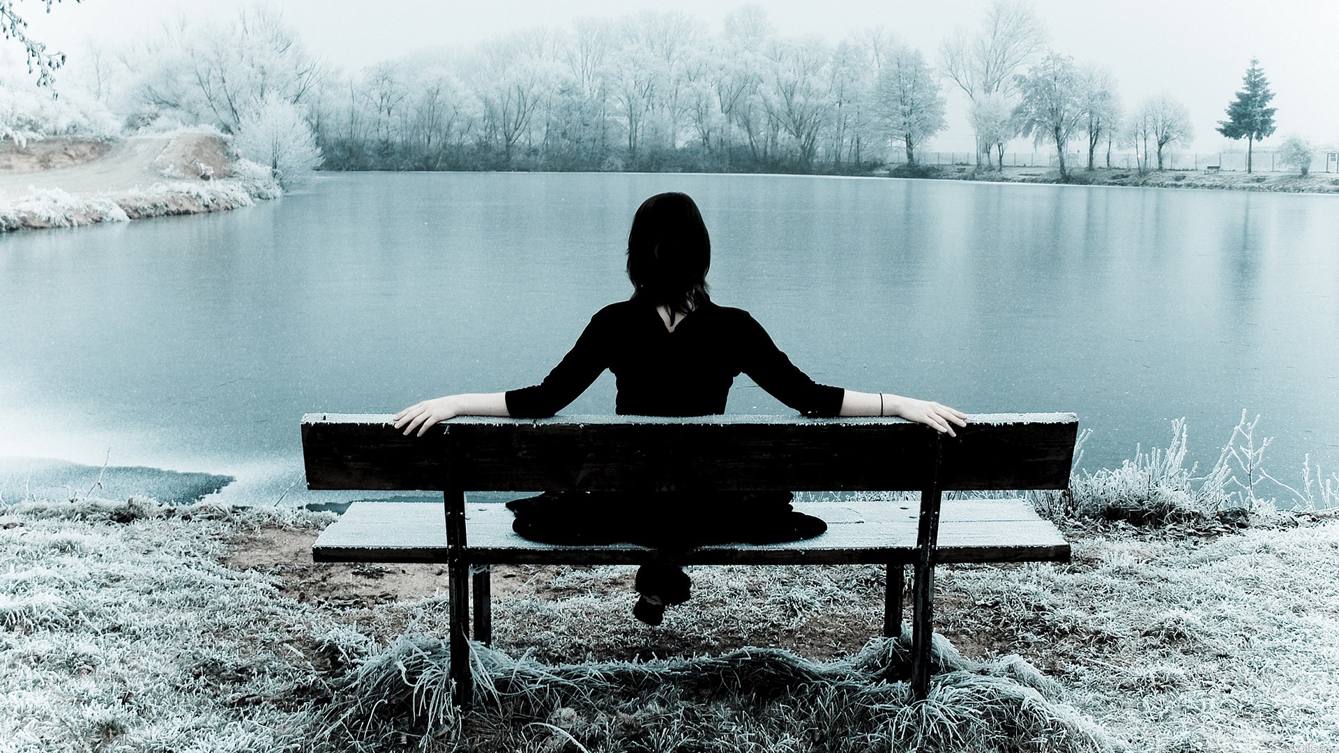 Woman in black sitting on a bench by a frozen lake HD Wallpaper