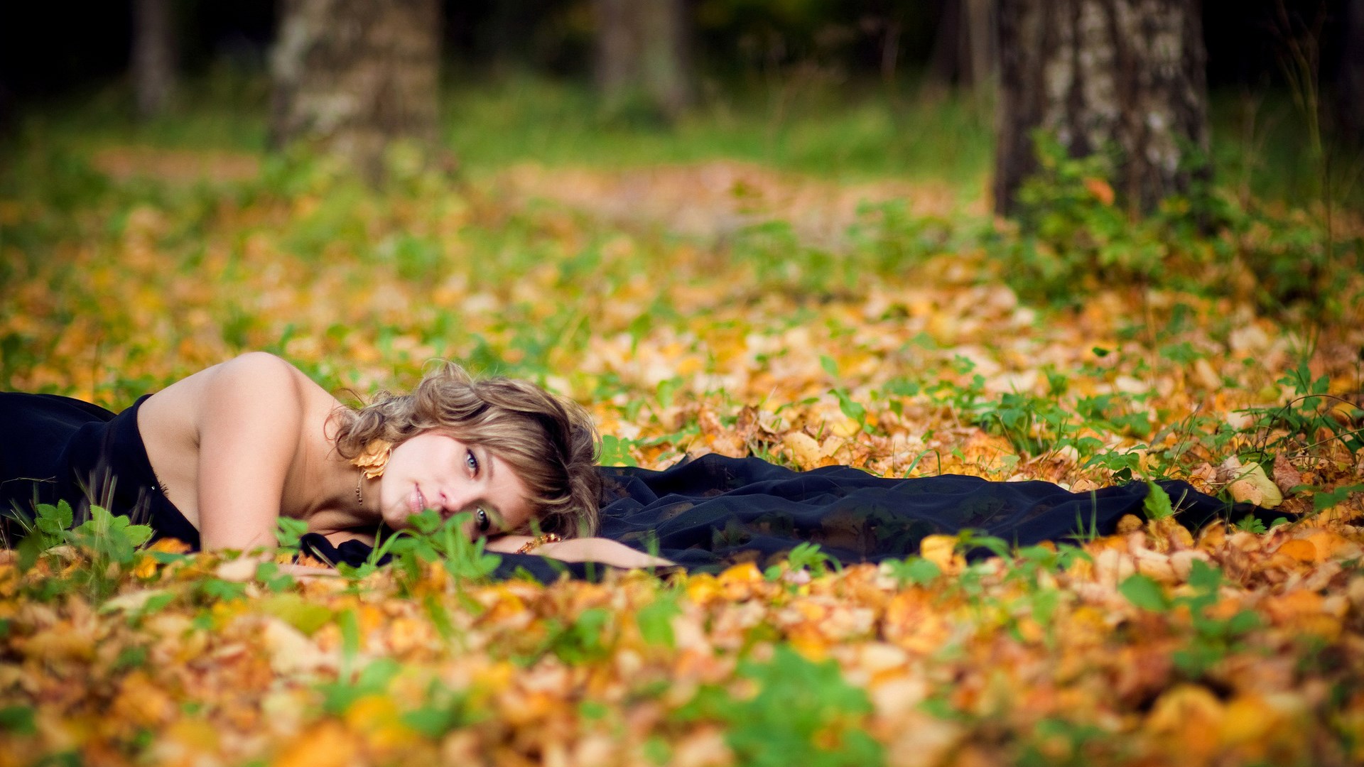 Woman lying on autumn leaves in a forest HD Wallpaper