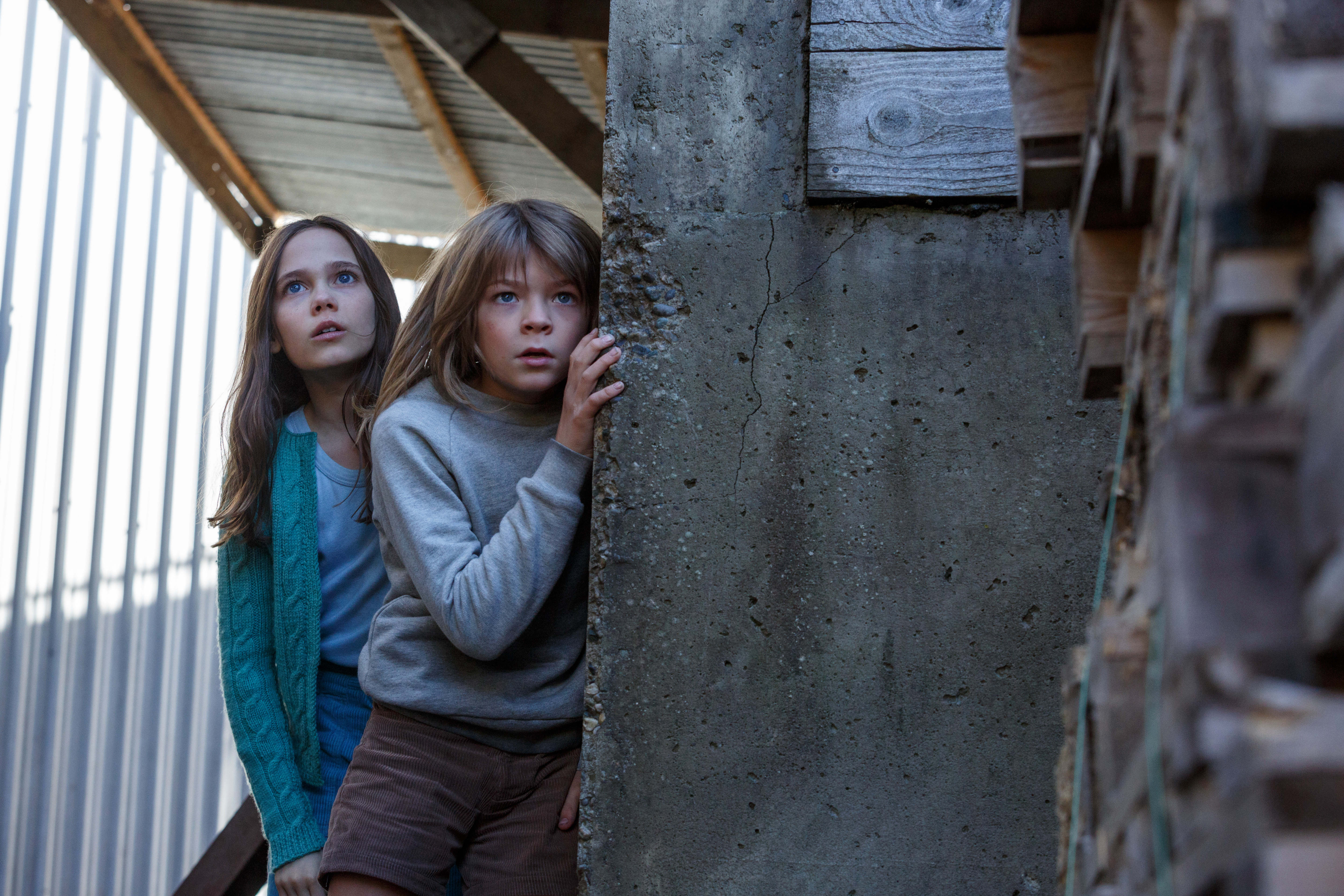 Two children hiding behind a concrete pillar HD Wallpaper