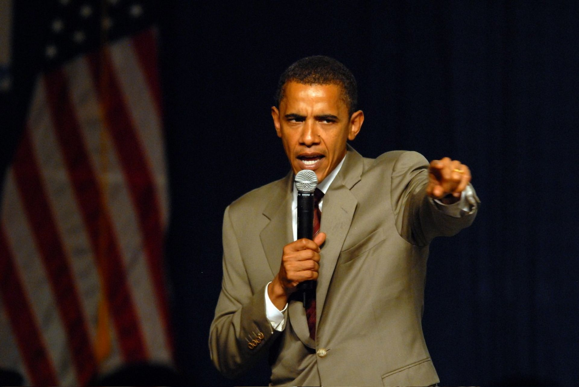 Barack Obama speaking at a podium with American flag HD Wallpaper