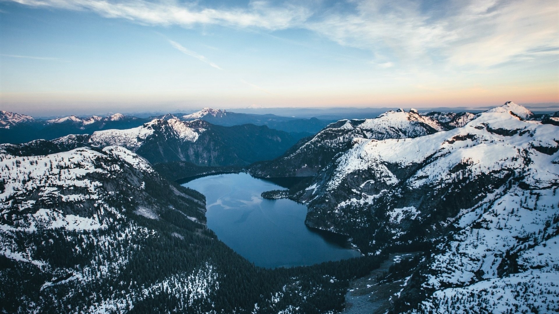 Snow-covered mountains surrounding a dark lake HD Wallpaper