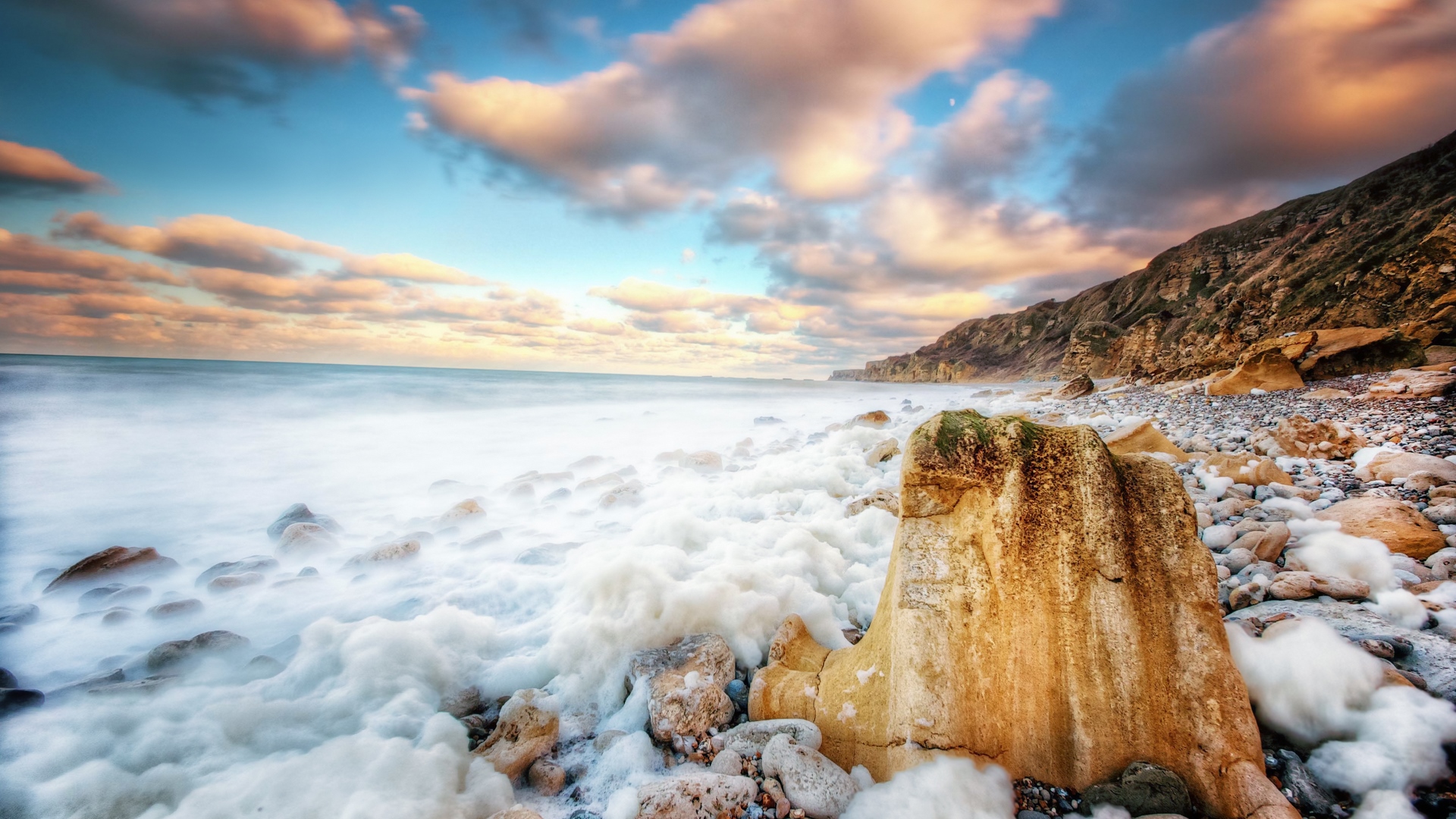 Foamy sea waves crash on a rocky beach at sunset HD Wallpaper