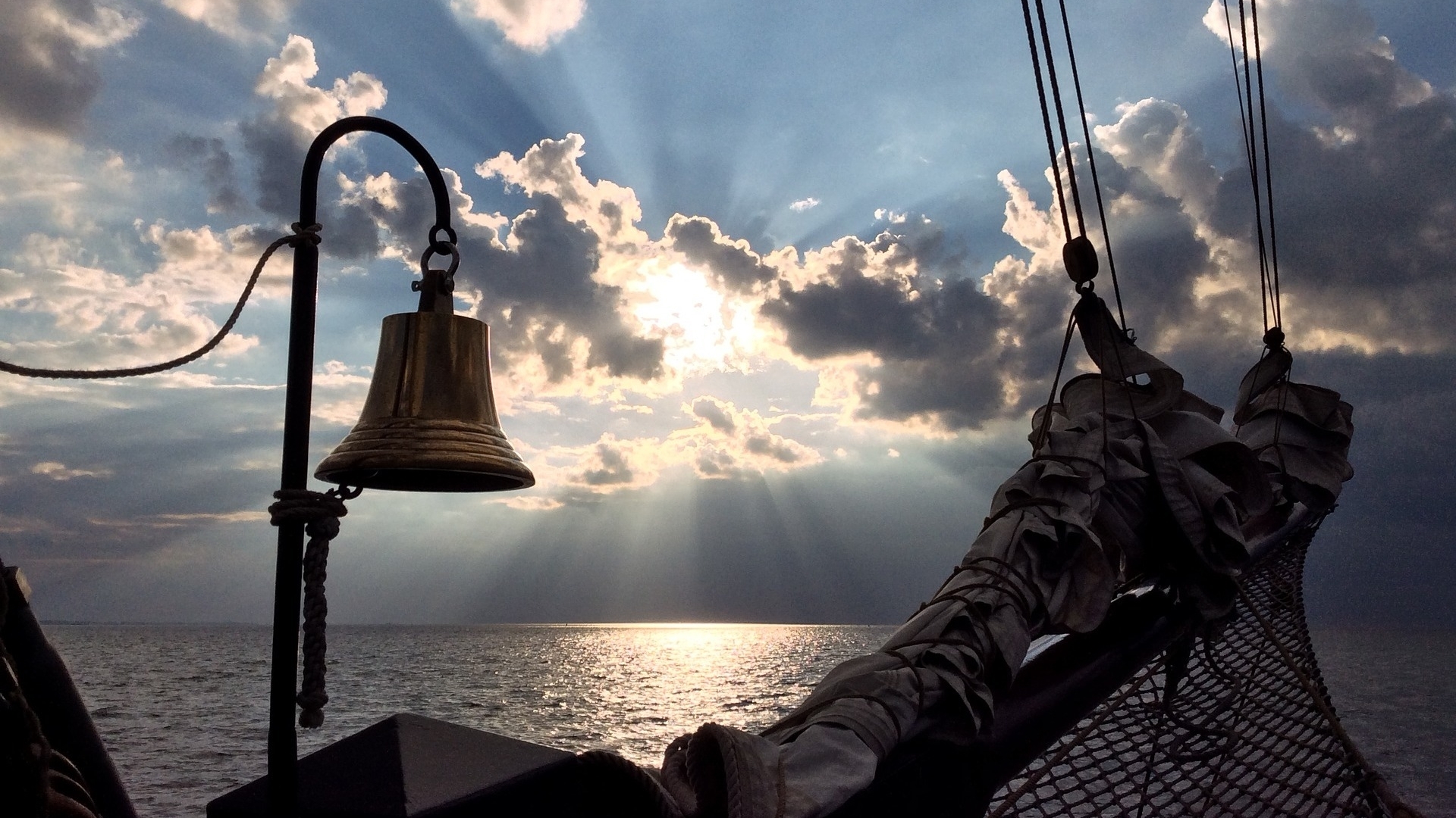 Ship's bell at sea with sunbeams through clouds HD Wallpaper
