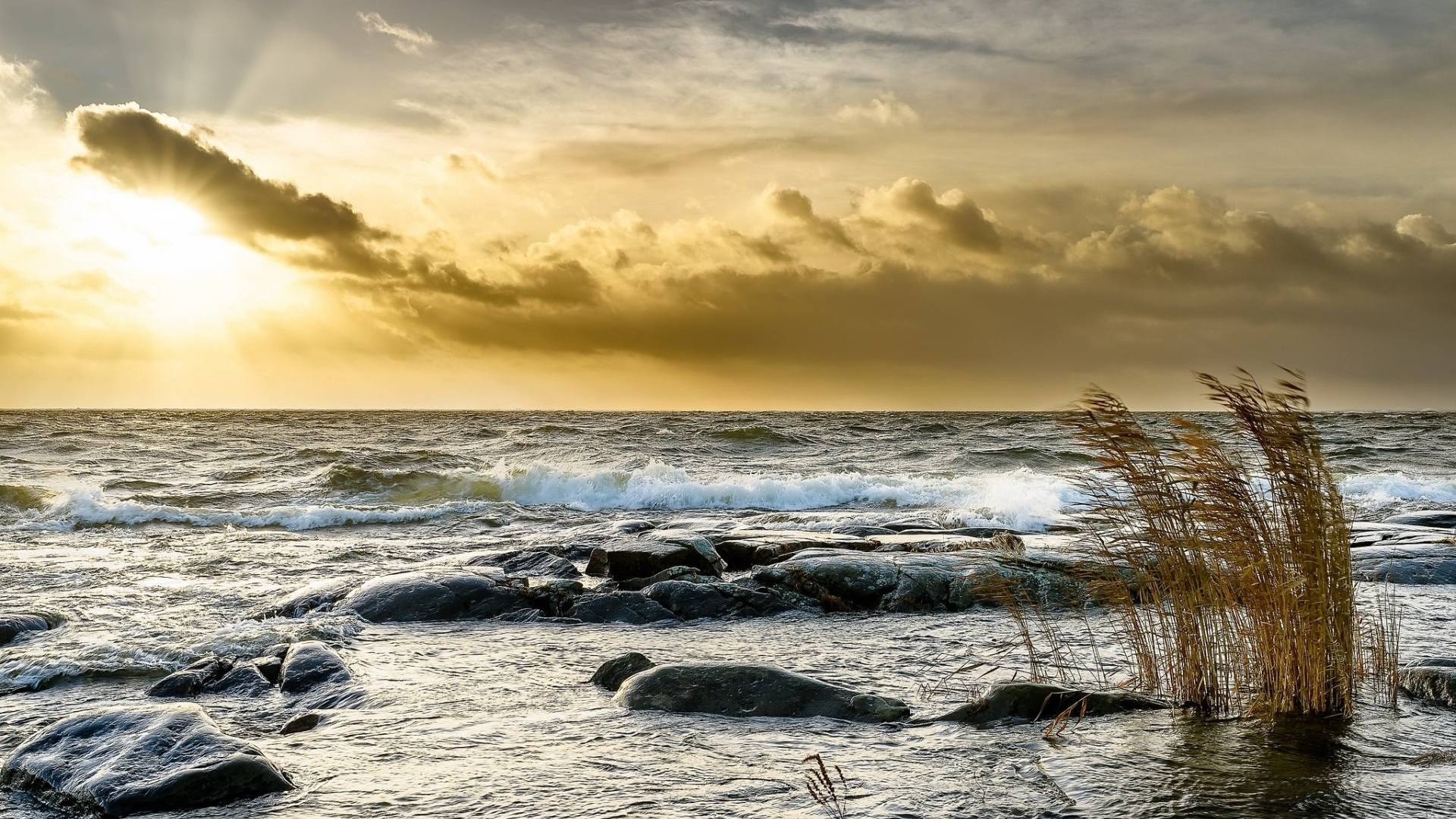 Sunlight breaking through clouds over rocky ocean shore HD Wallpaper
