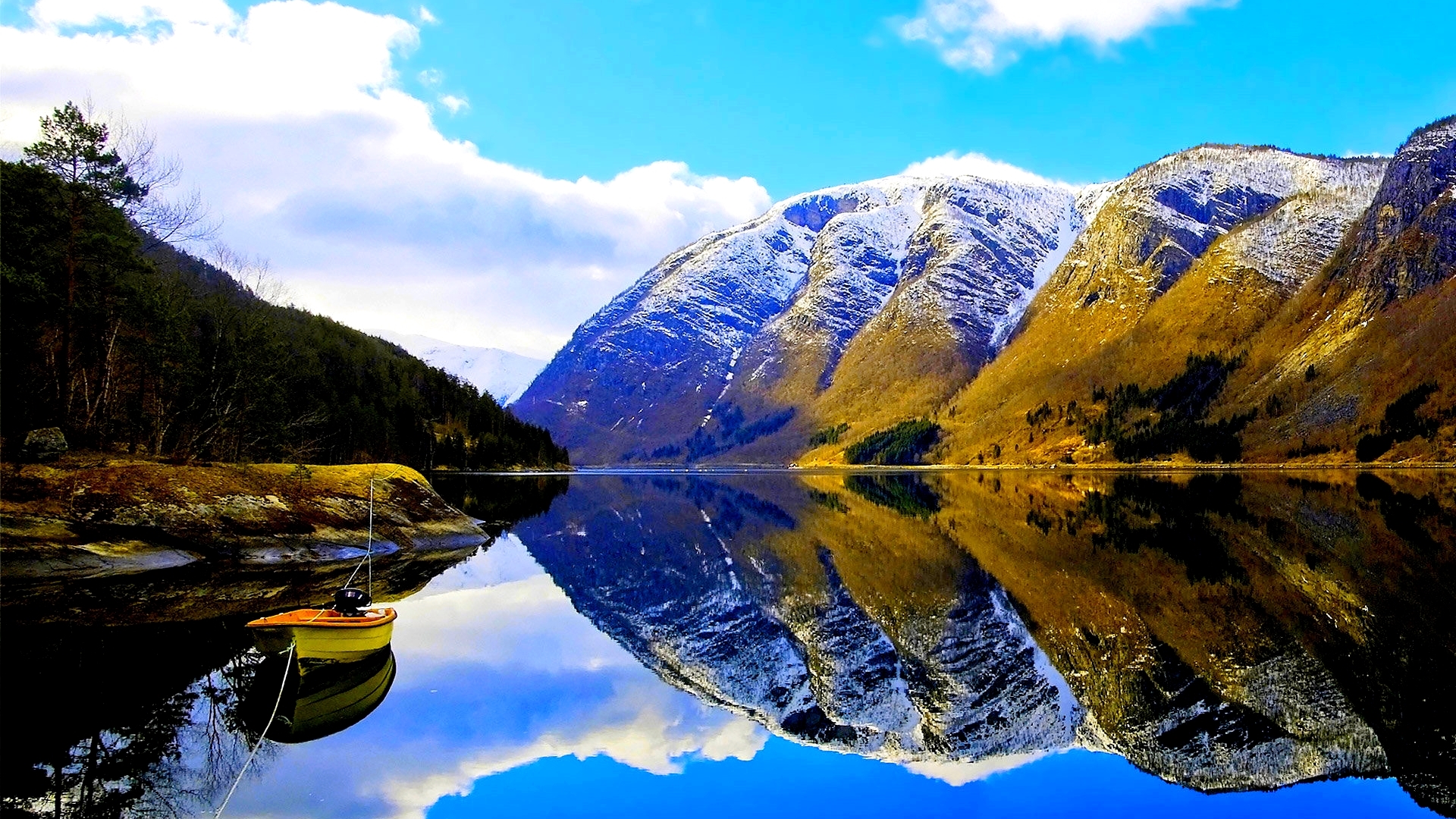 Snow-capped mountains reflected in a calm lake with a boat HD Wallpaper