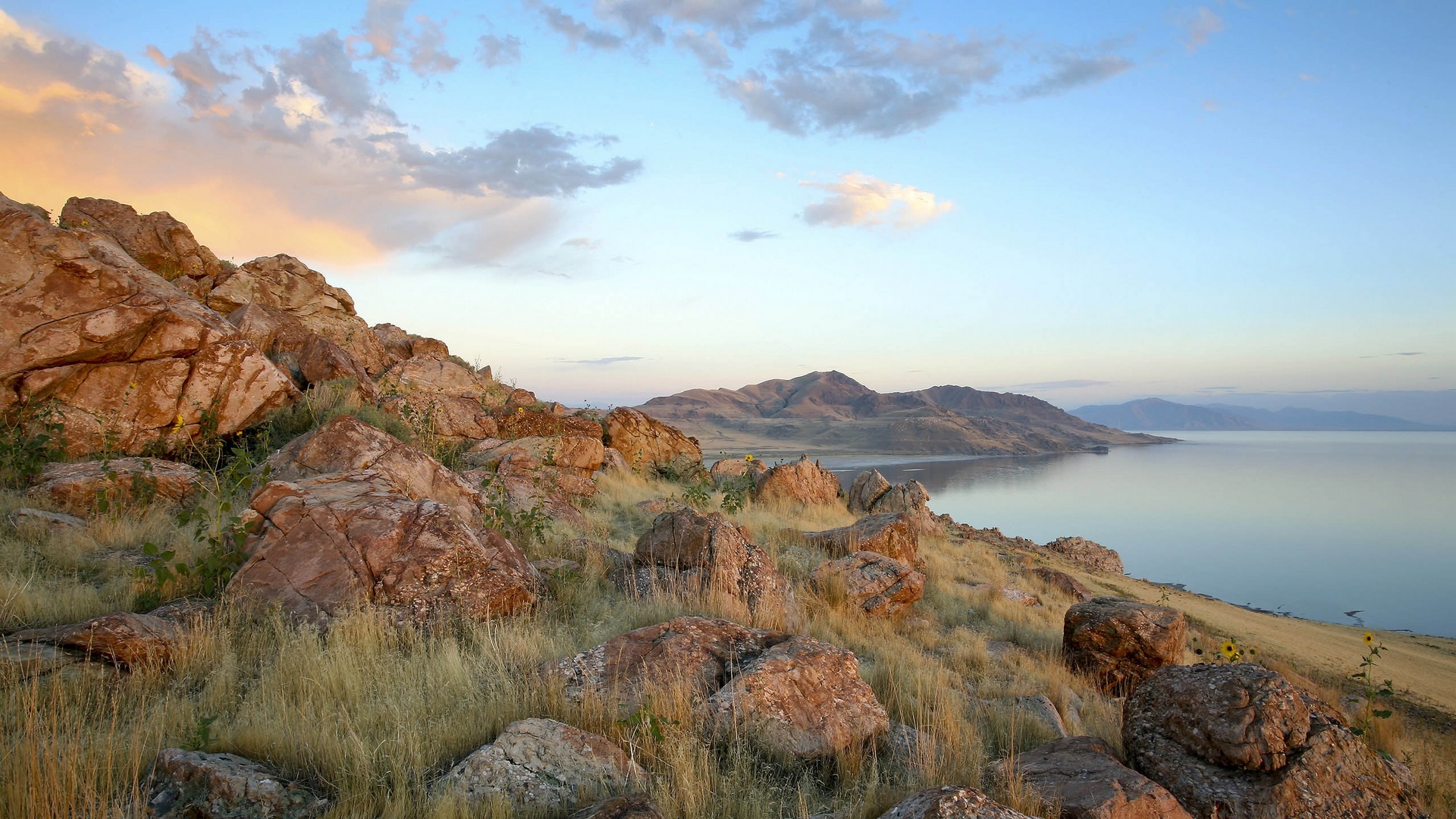 Rocky shore overlooking a calm lake and distant mountains HD Wallpaper