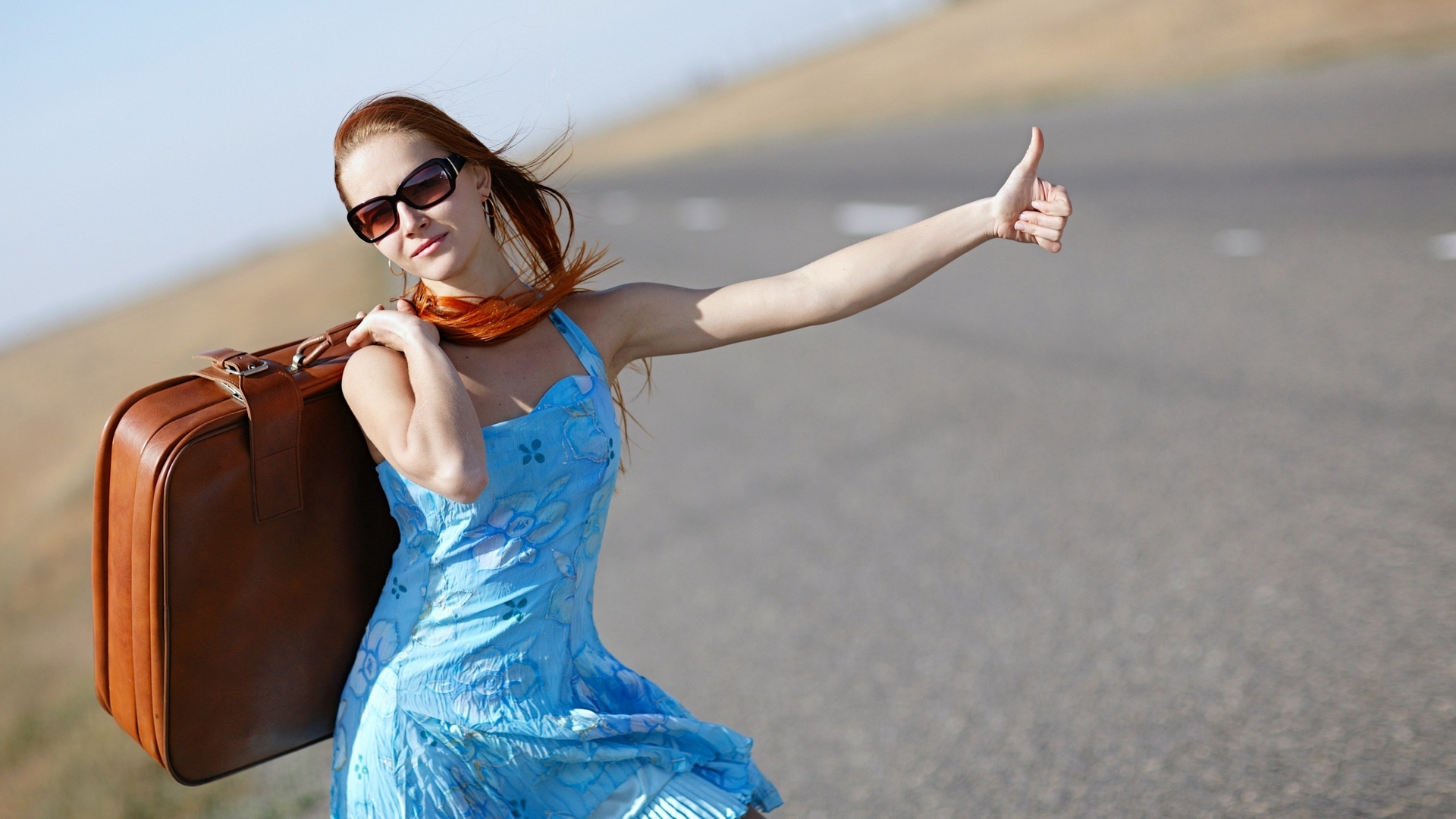 Redhead woman with suitcase hitchhiking on a road HD Wallpaper