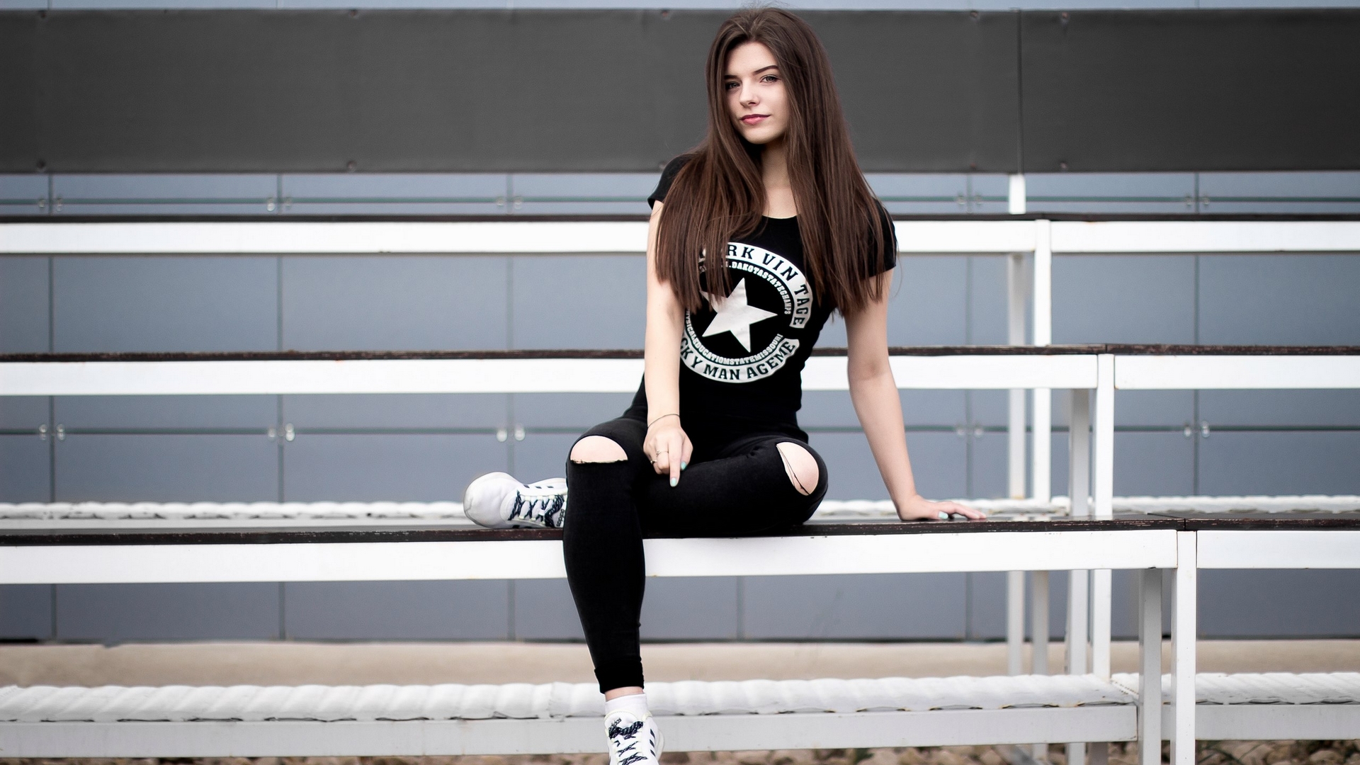 Young woman in ripped jeans sitting on bleachers HD Wallpaper