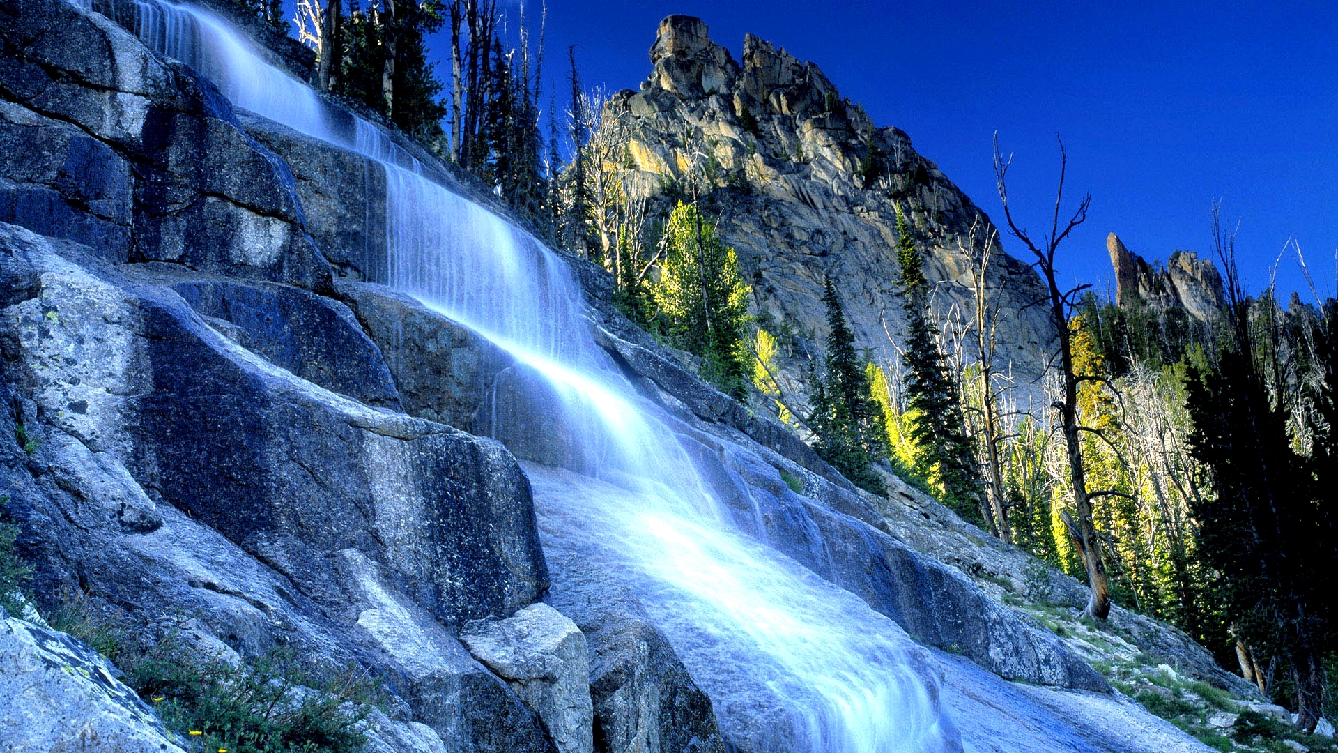 Waterfall cascading down a rocky mountain with trees HD Wallpaper