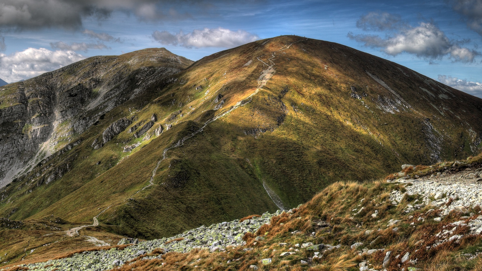 Mountain range with hiking trail under cloudy sky HD Wallpaper