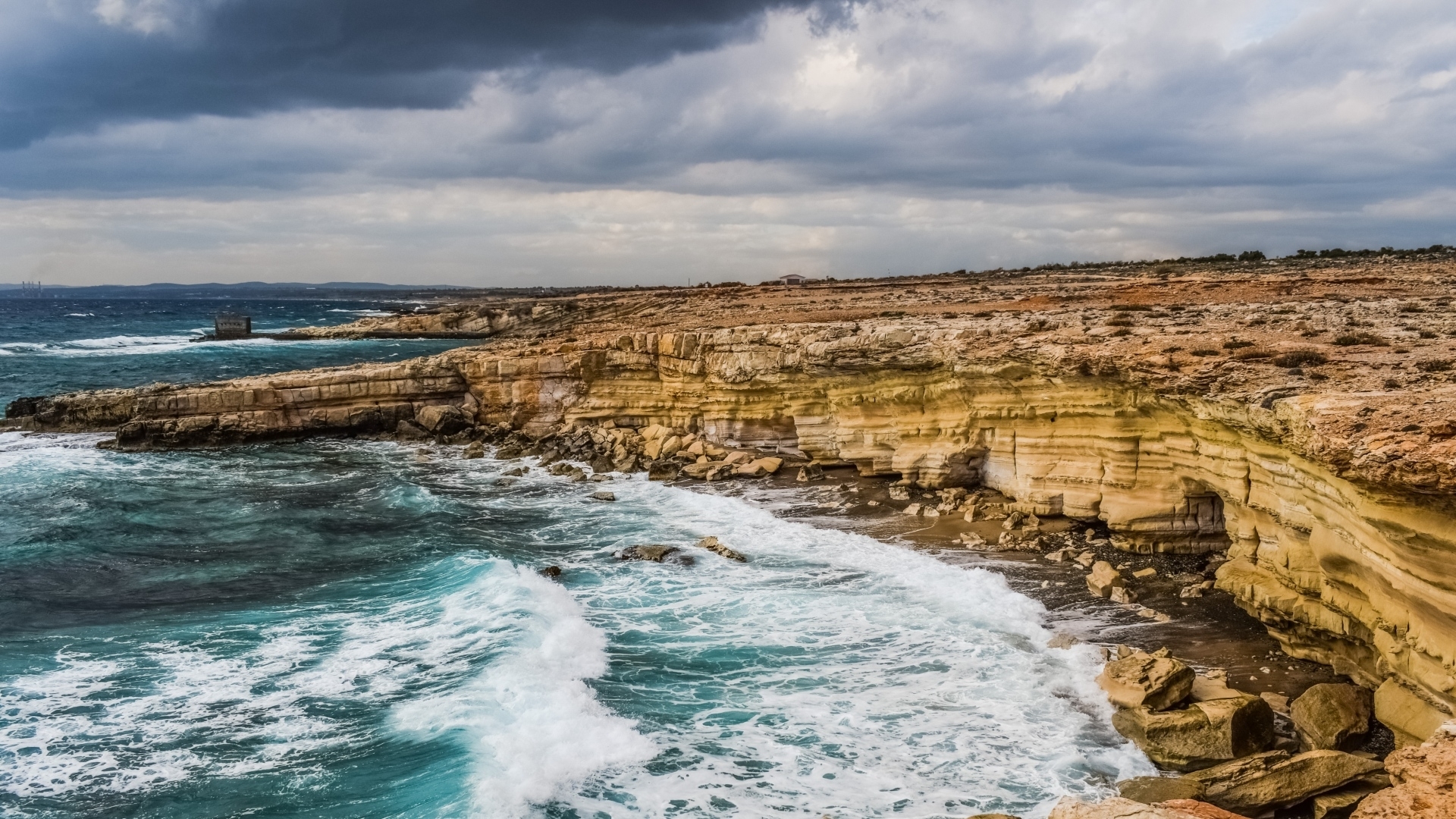 Rocky coastline with crashing waves under a cloudy sky HD Wallpaper
