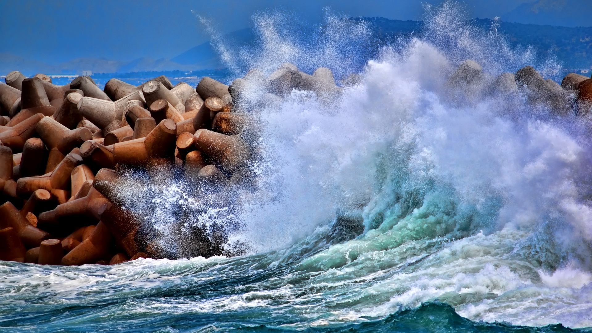 Waves crashing against tetrapods on a sunny day HD Wallpaper