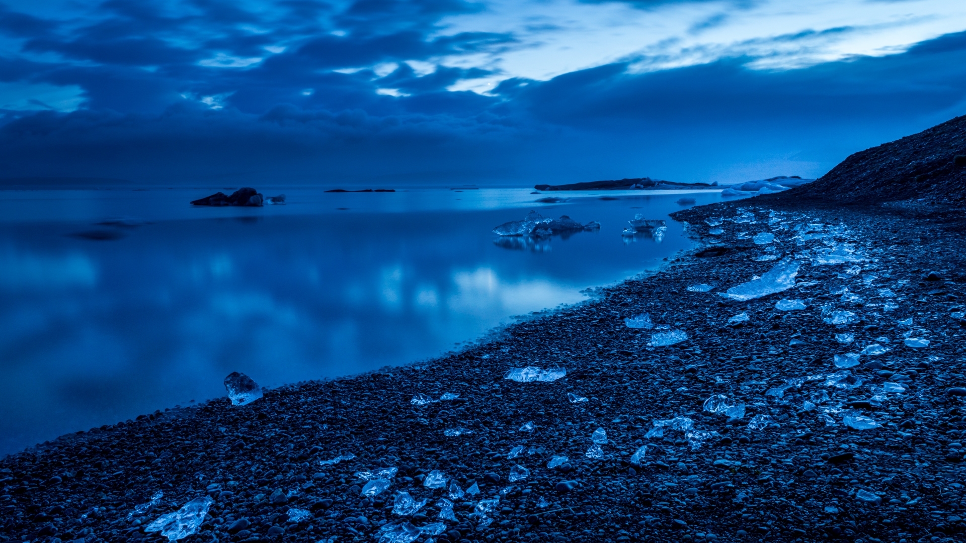 Blue icebergs on a rocky shore with calm ocean and cloudy sky HD Wallpaper