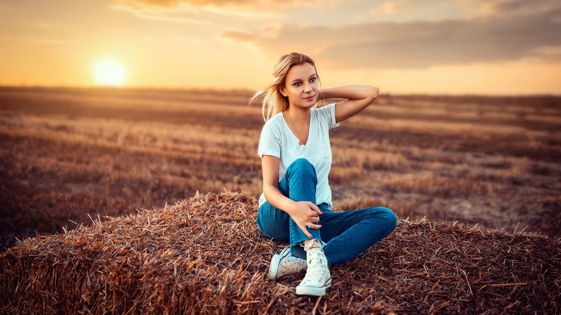 Woman in jeans sitting on hay bale at sunset HD Wallpaper