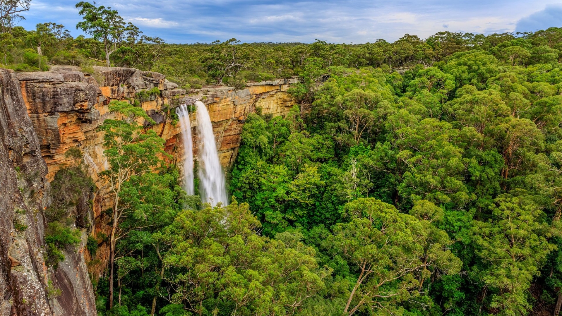 Waterfall cascading down a cliff surrounded by forest HD Wallpaper