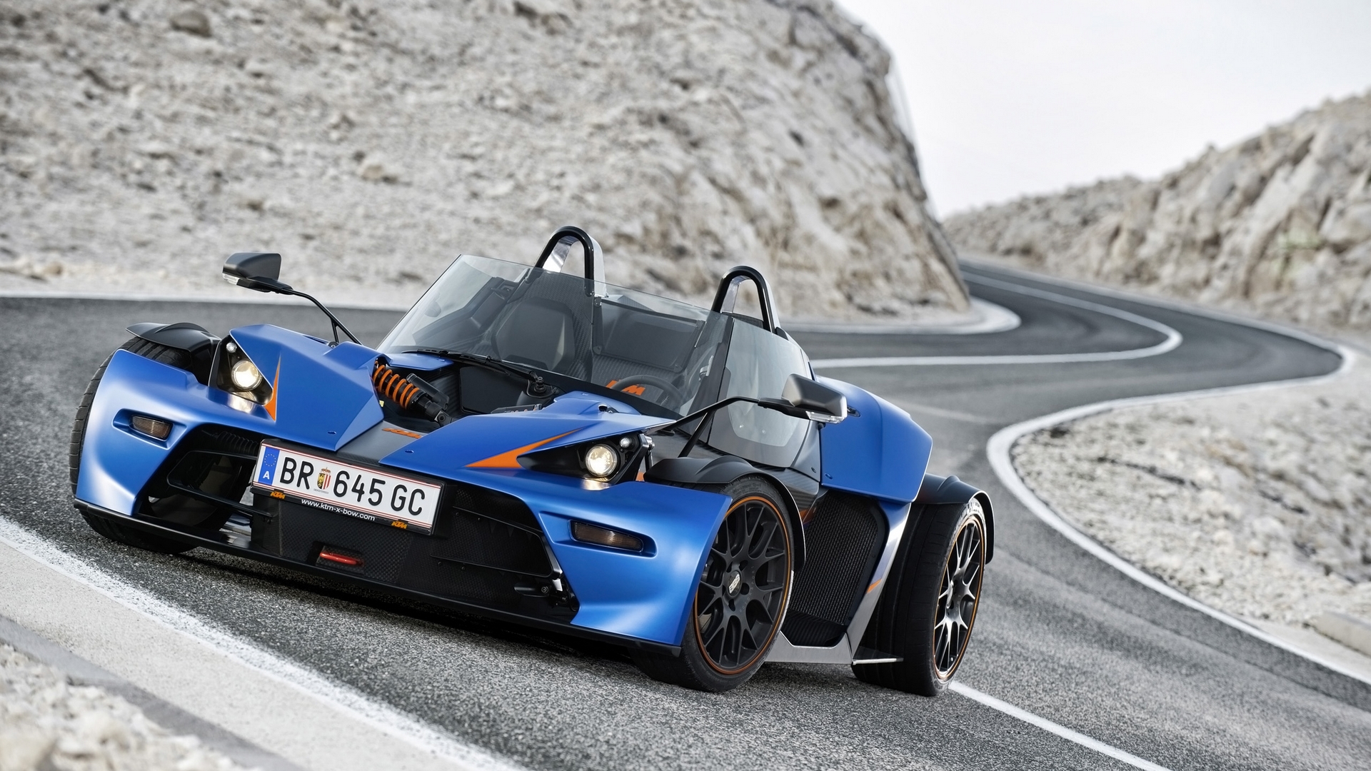 Blue KTM X-Bow driving on a winding mountain road HD Wallpaper