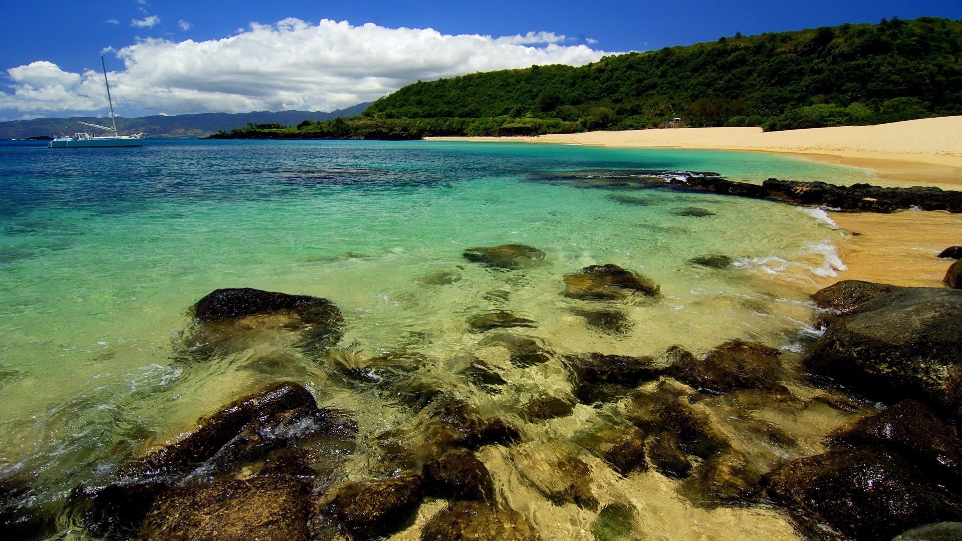 Turquoise ocean water with rocks and a sandy beach HD Wallpaper