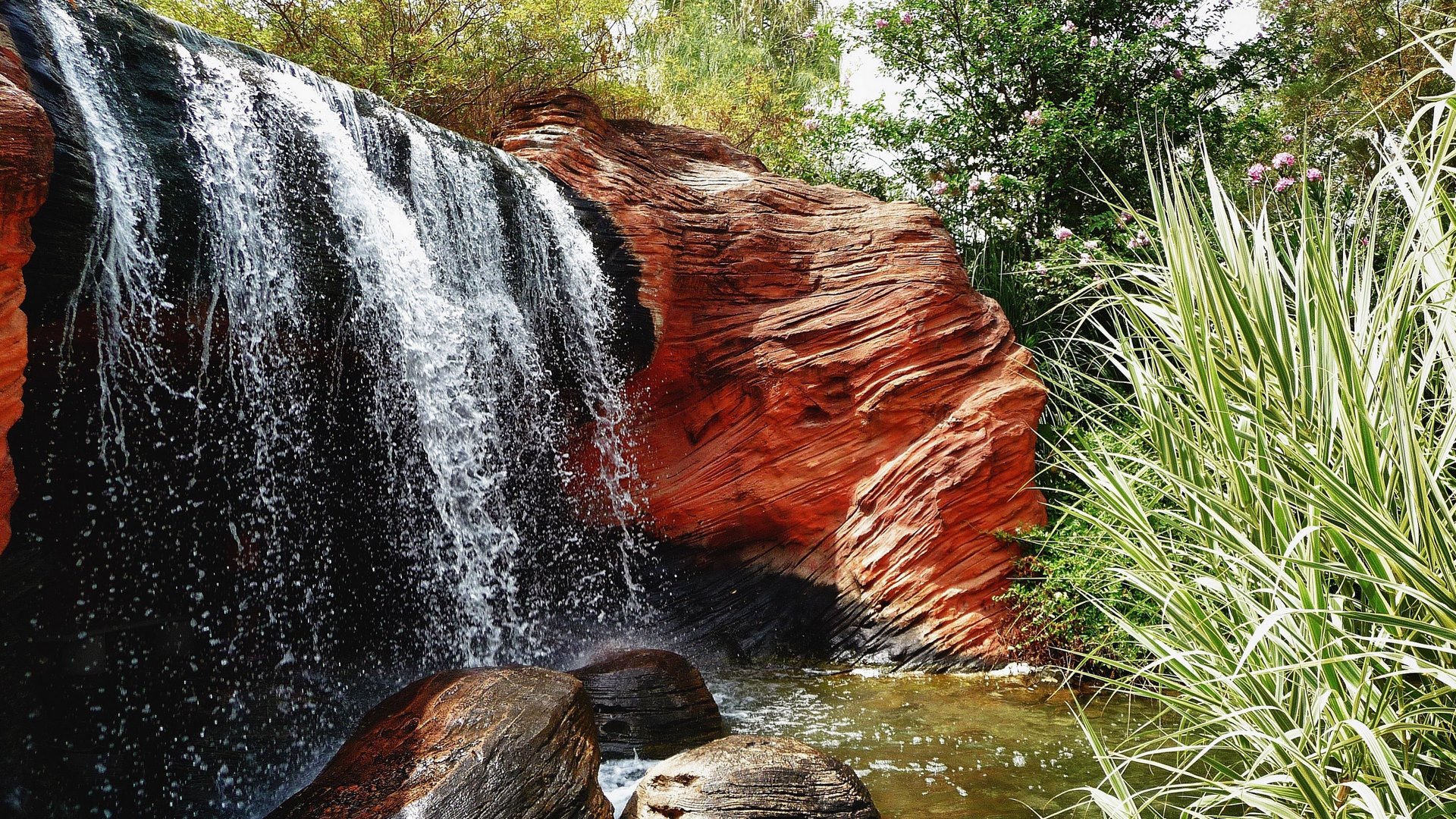 Waterfall cascading over red rocks with lush greenery HD Wallpaper