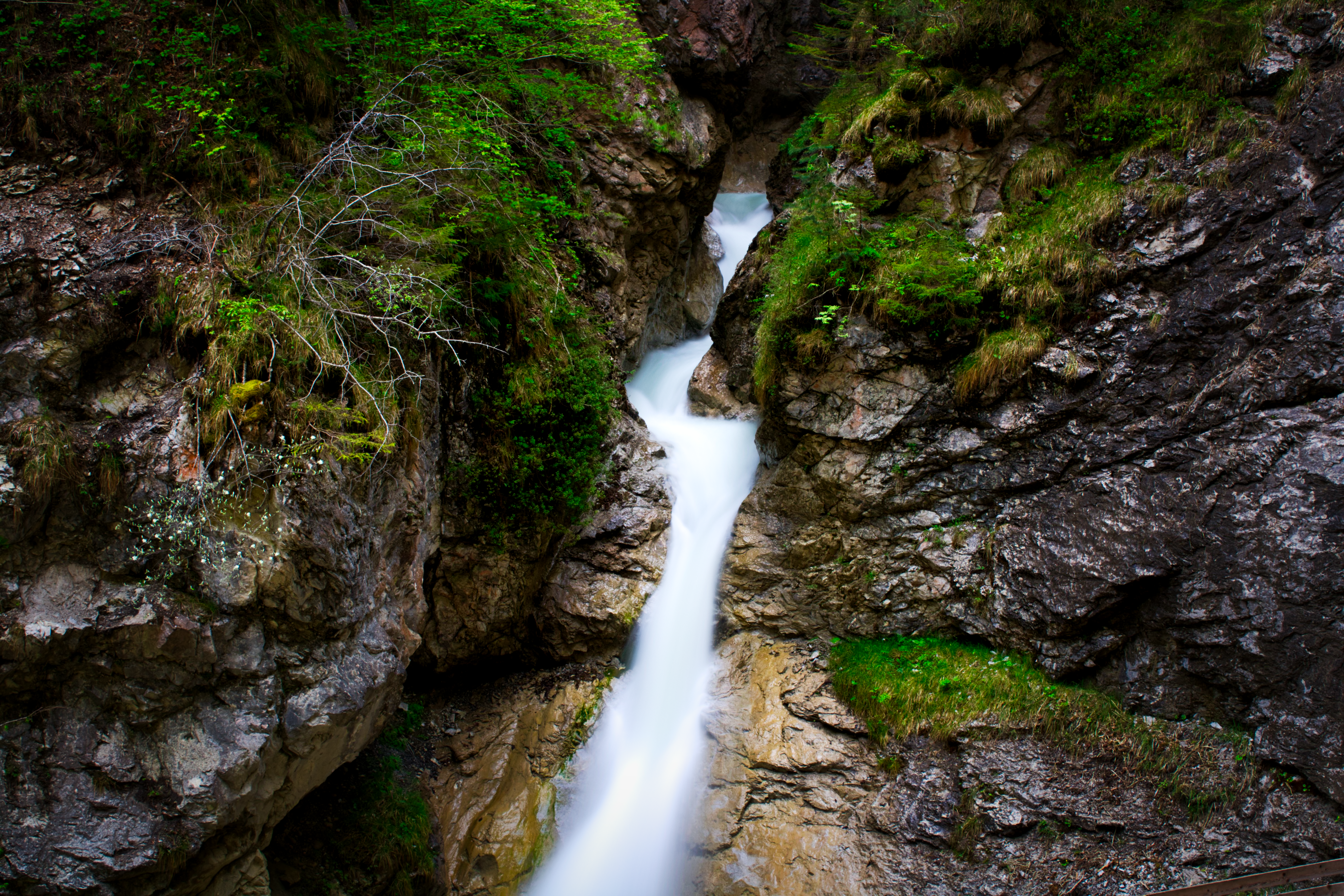 Waterfall flowing through a rocky gorge with greenery HD Wallpaper