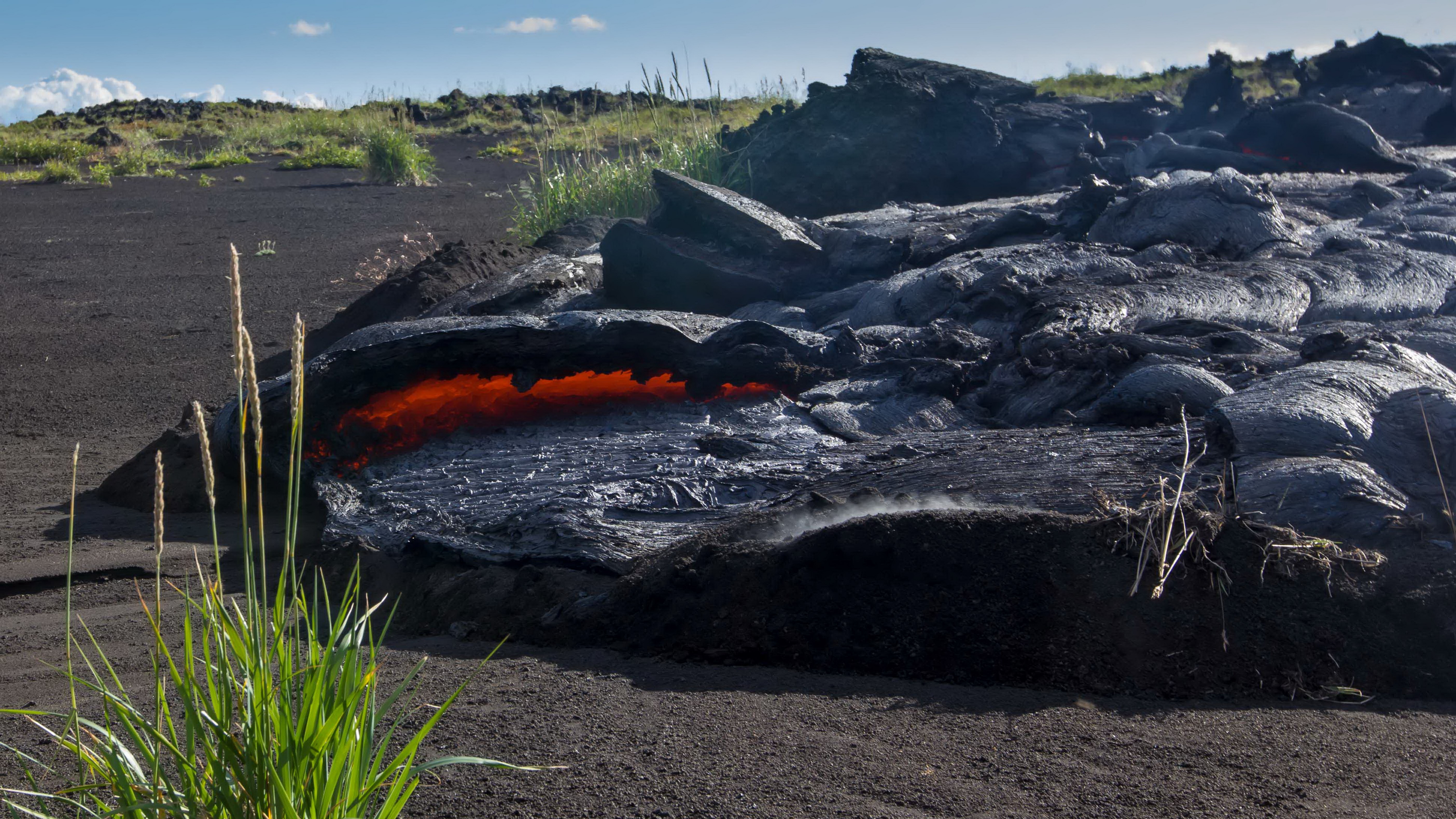 Molten lava flowing over black volcanic rock and sand HD Wallpaper
