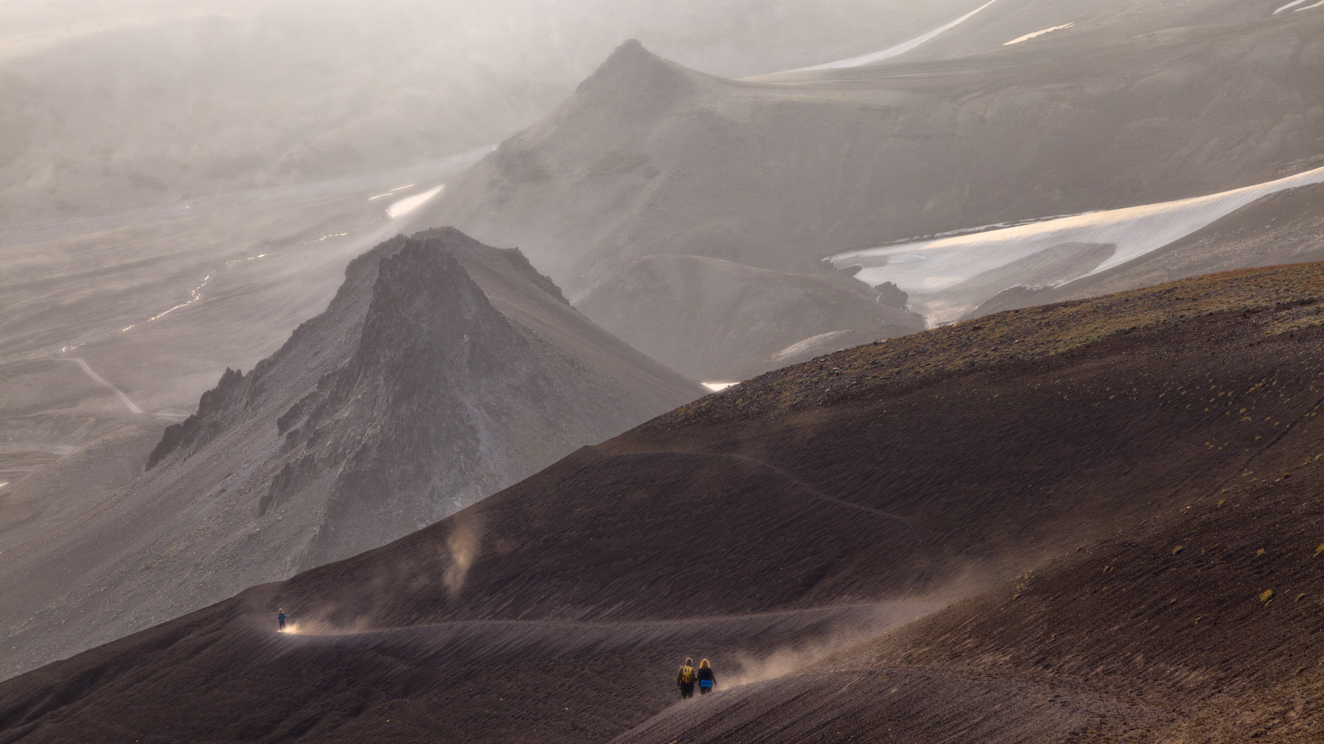 Hikers on a dusty mountain trail with volcanic peaks HD Wallpaper