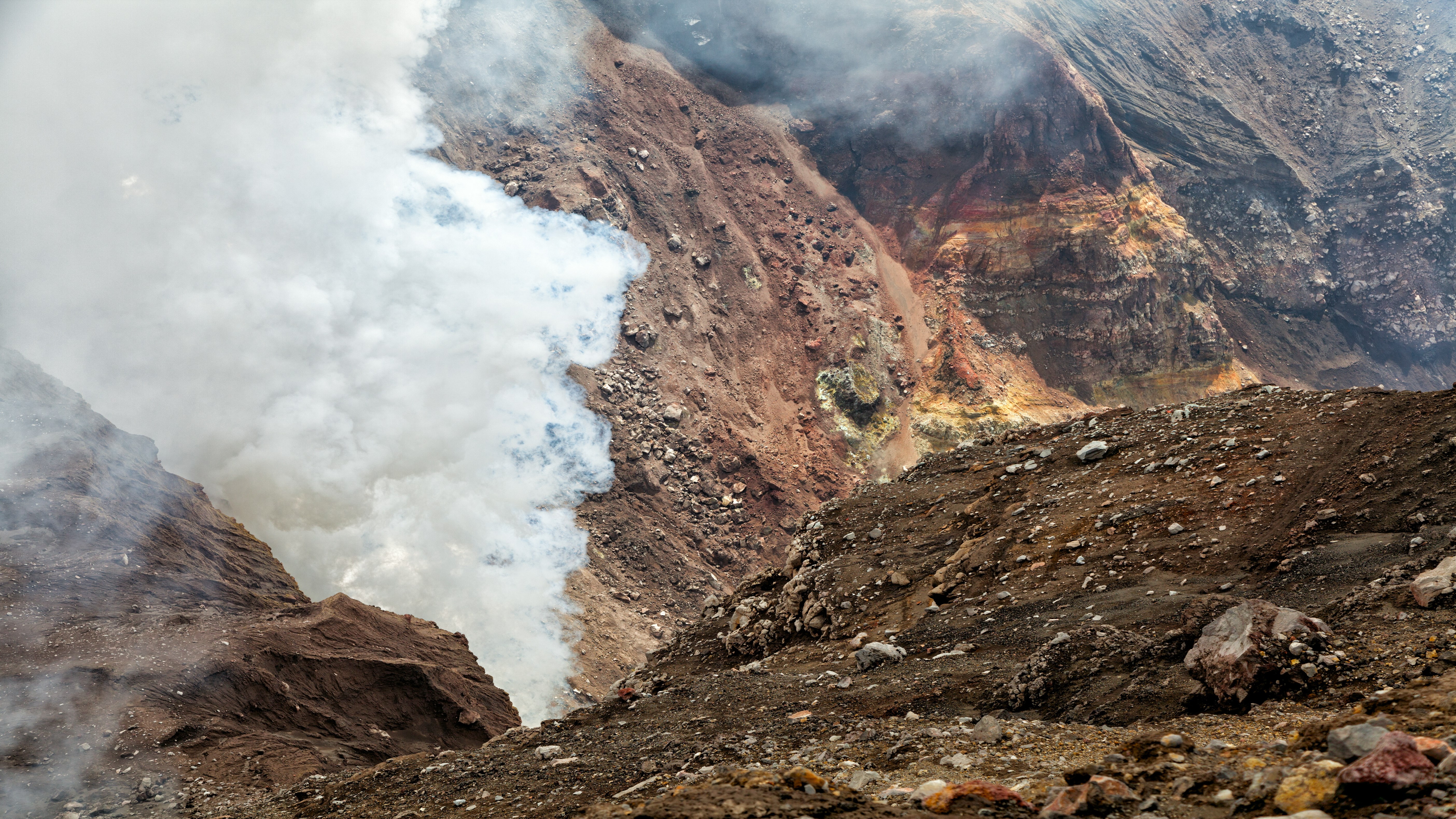 Volcanic crater with steam and rocky terrain HD Wallpaper