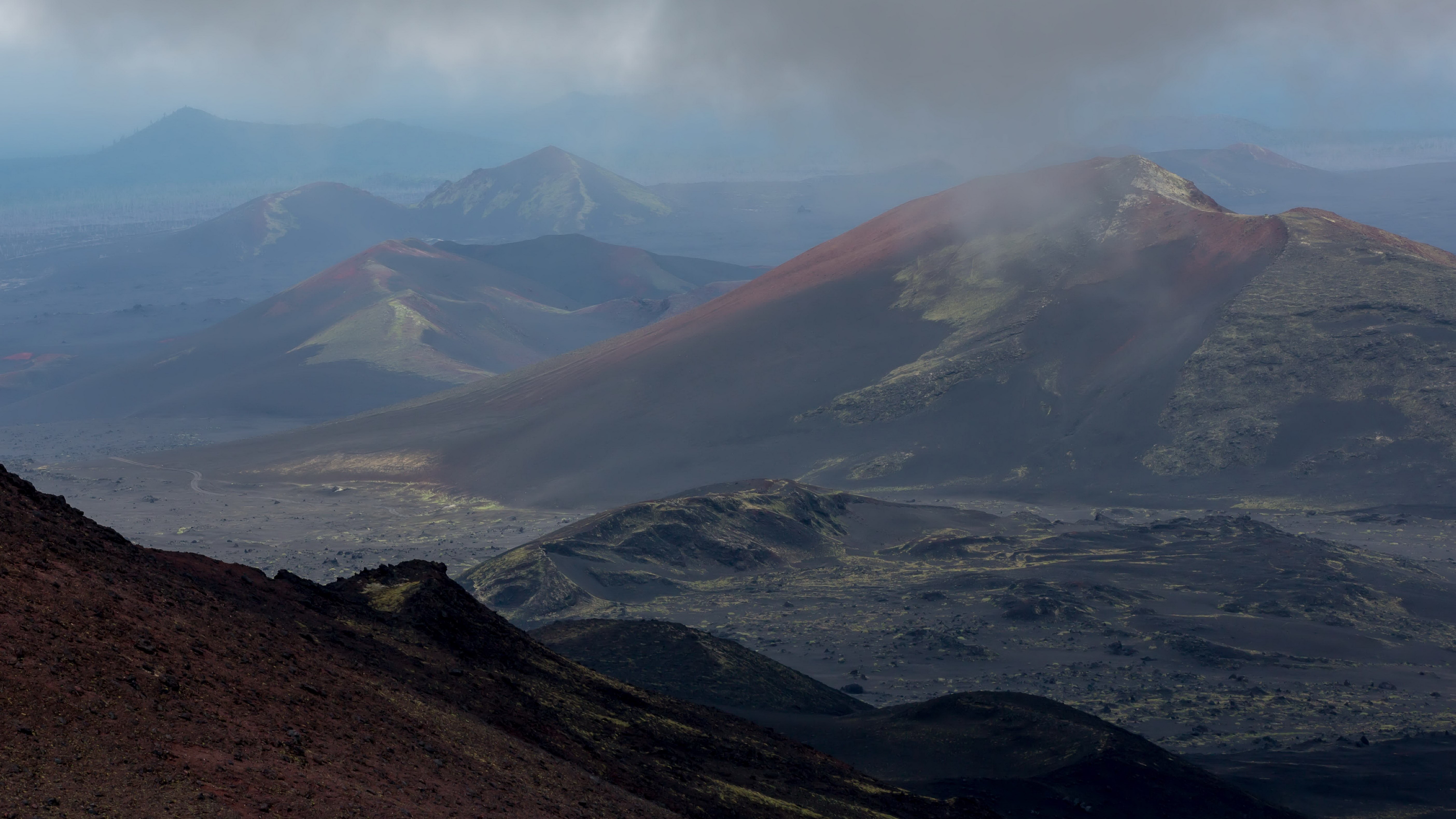 Volcanic landscape with red-capped mountains and clouds HD Wallpaper