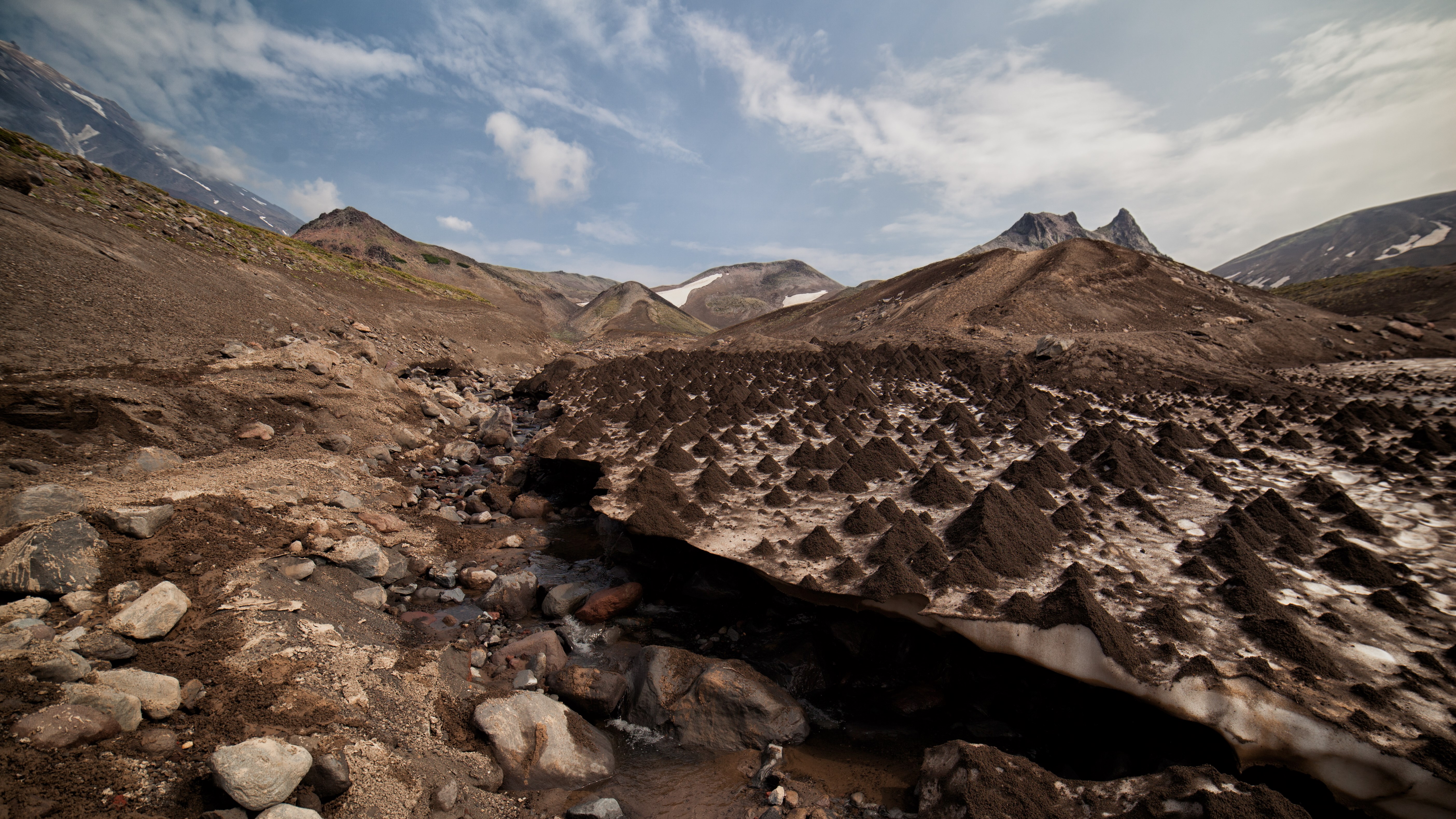 Volcanic landscape with snow-capped mountains and a stream HD Wallpaper