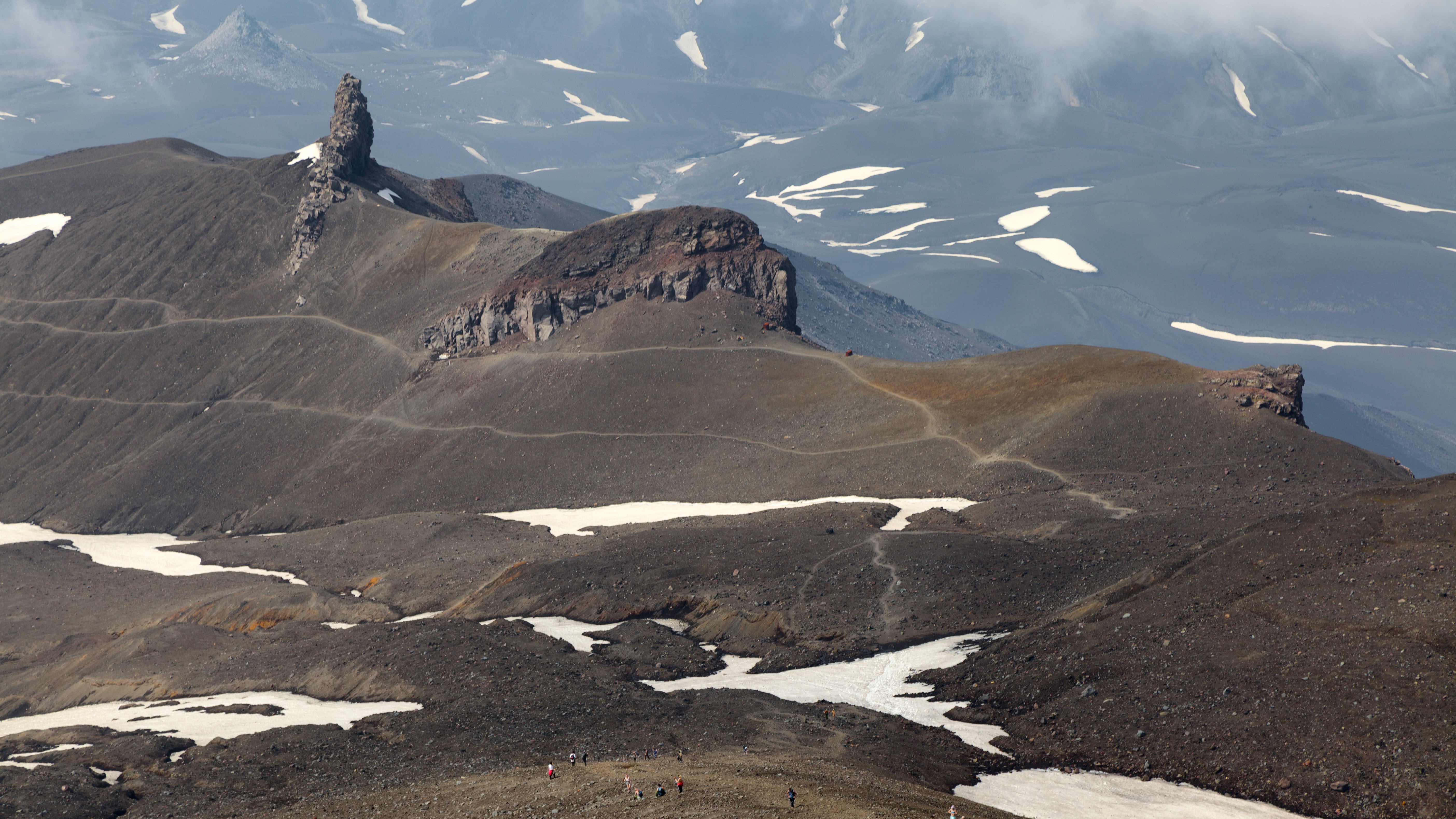 Volcanic landscape with rocky outcrops and snow patches HD Wallpaper
